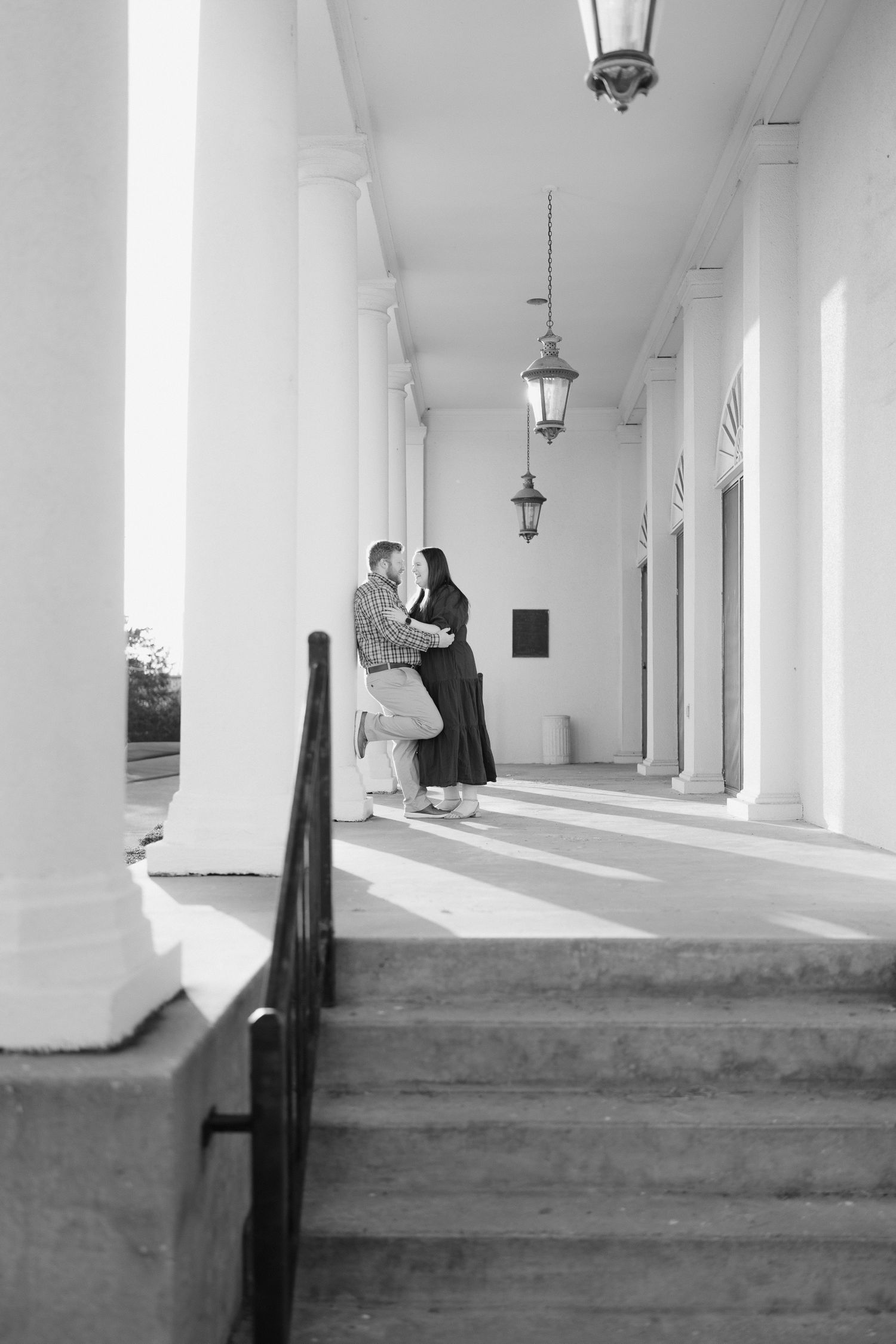 Black and white photo of a couple sharing a romantic moment on steps between white columns of a historic building.
