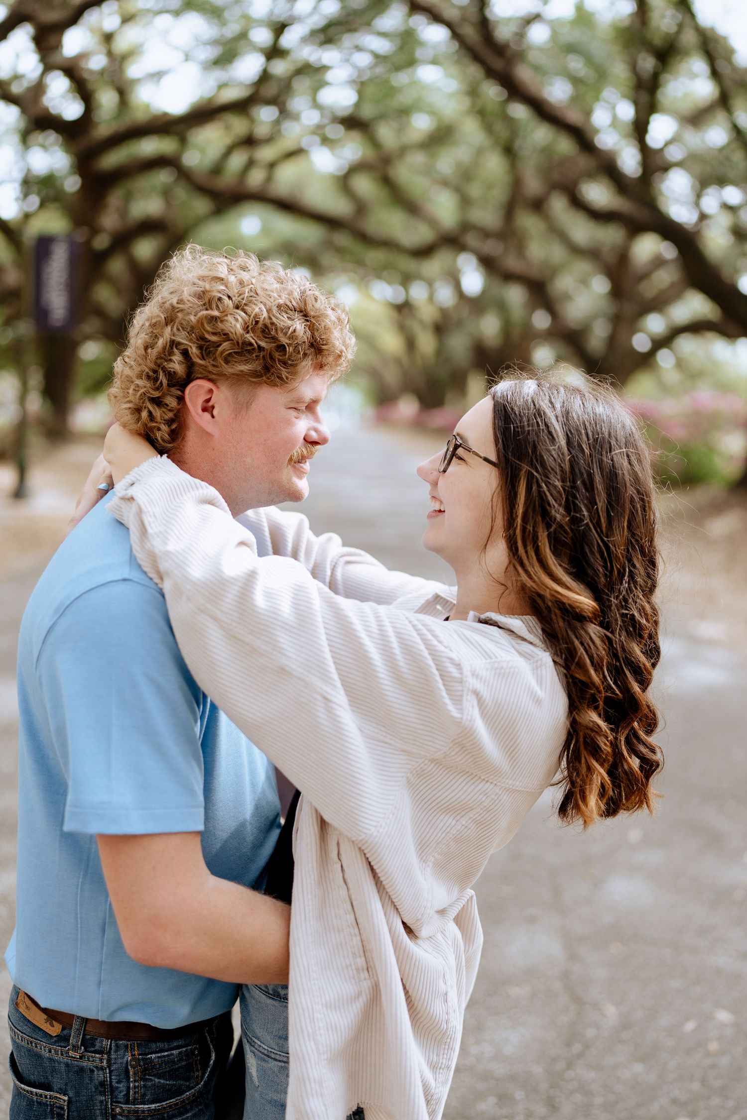 A couple sharing a romantic embrace under oak trees in a park setting.