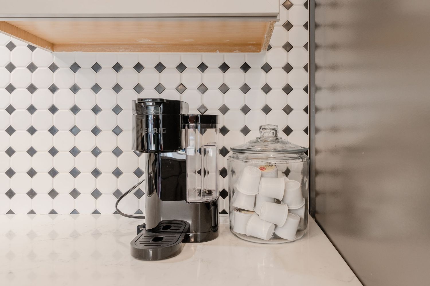 Minimalist white kitchen counter with small appliances and a geometric tile backsplash pattern.