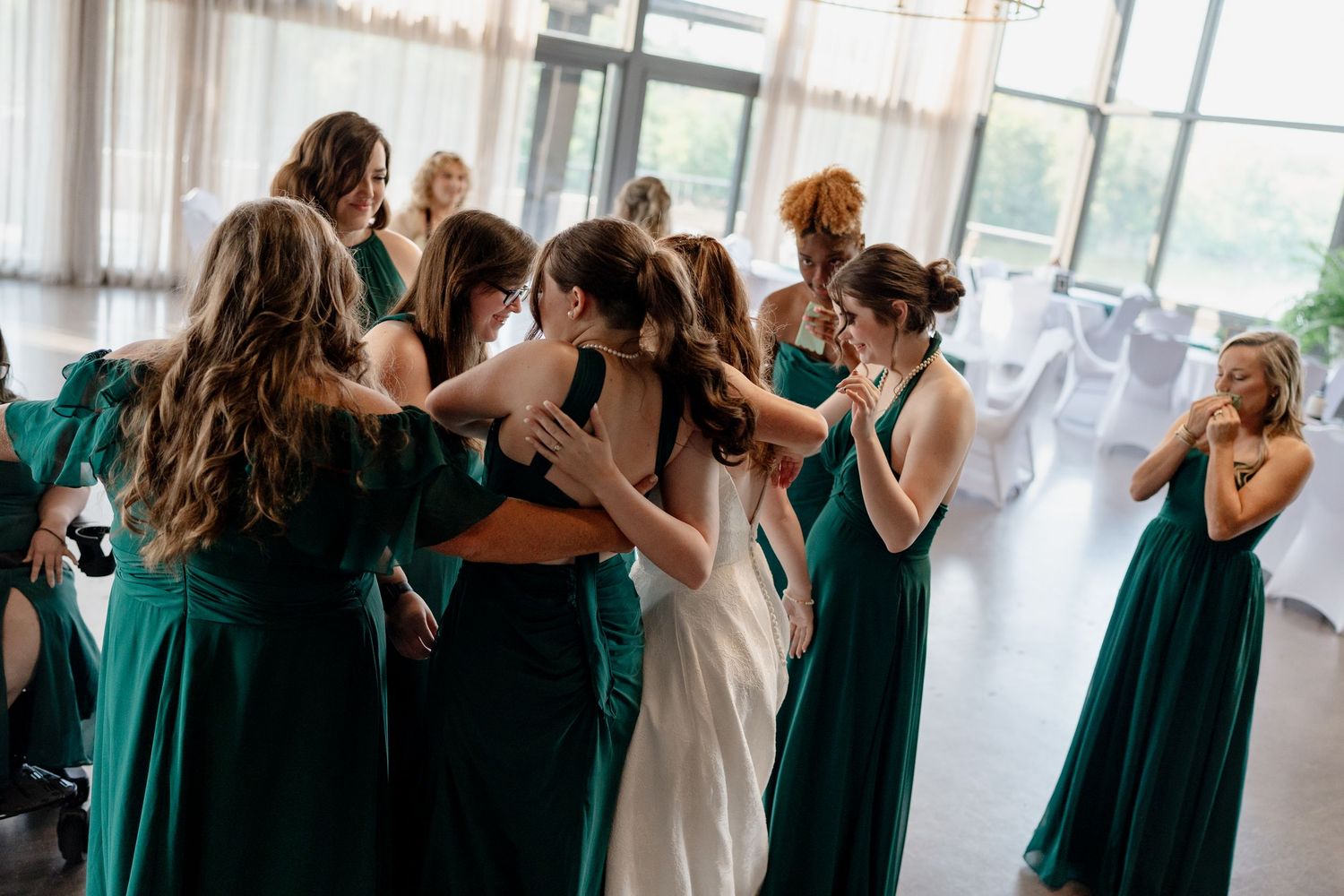 Bridesmaids in emerald green dresses gather in an emotional group moment during a wedding celebration.