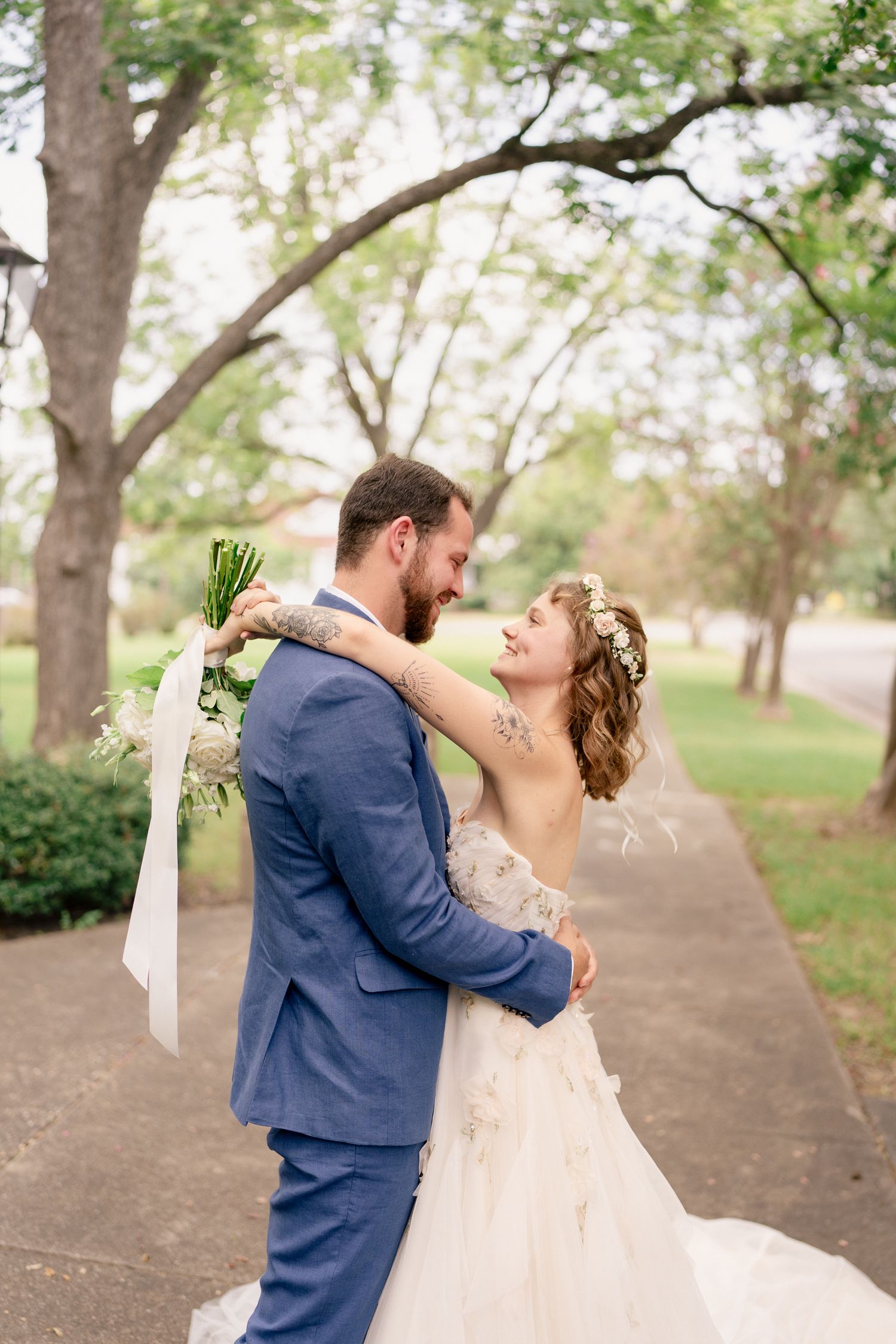 A romantic wedding couple shares an intimate dance moment in a tree-lined outdoor setting.