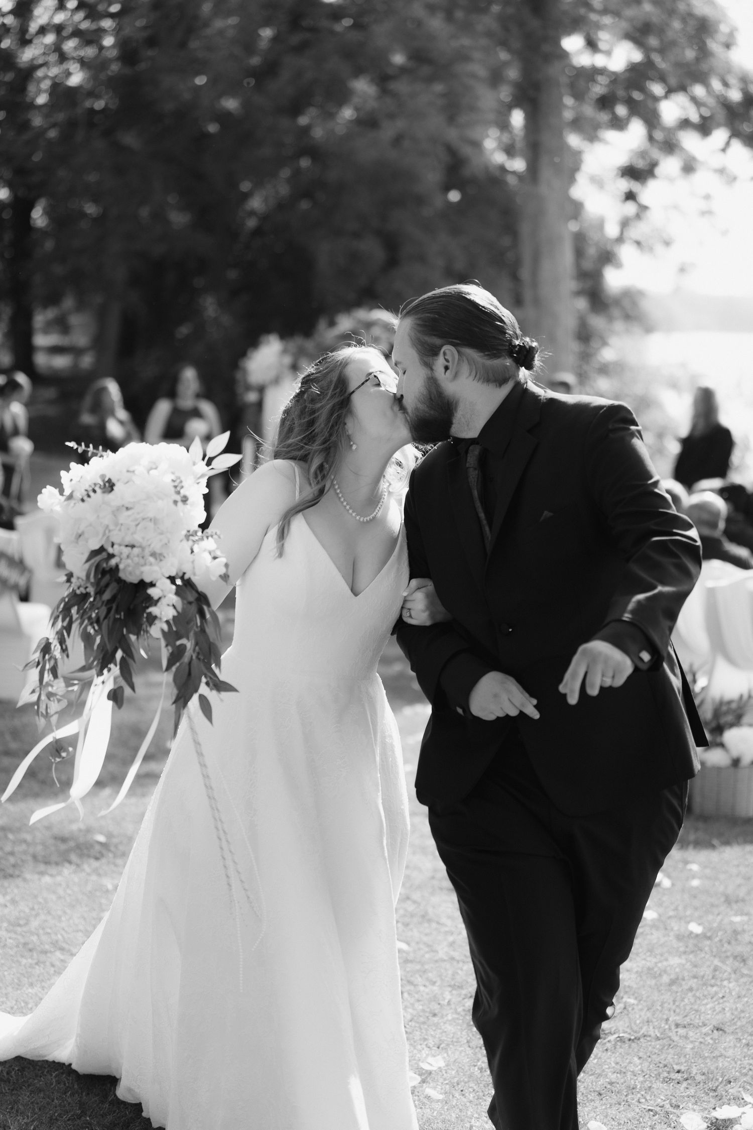 A romantic black and white wedding photograph of a couple sharing a tender moment outdoors under trees.