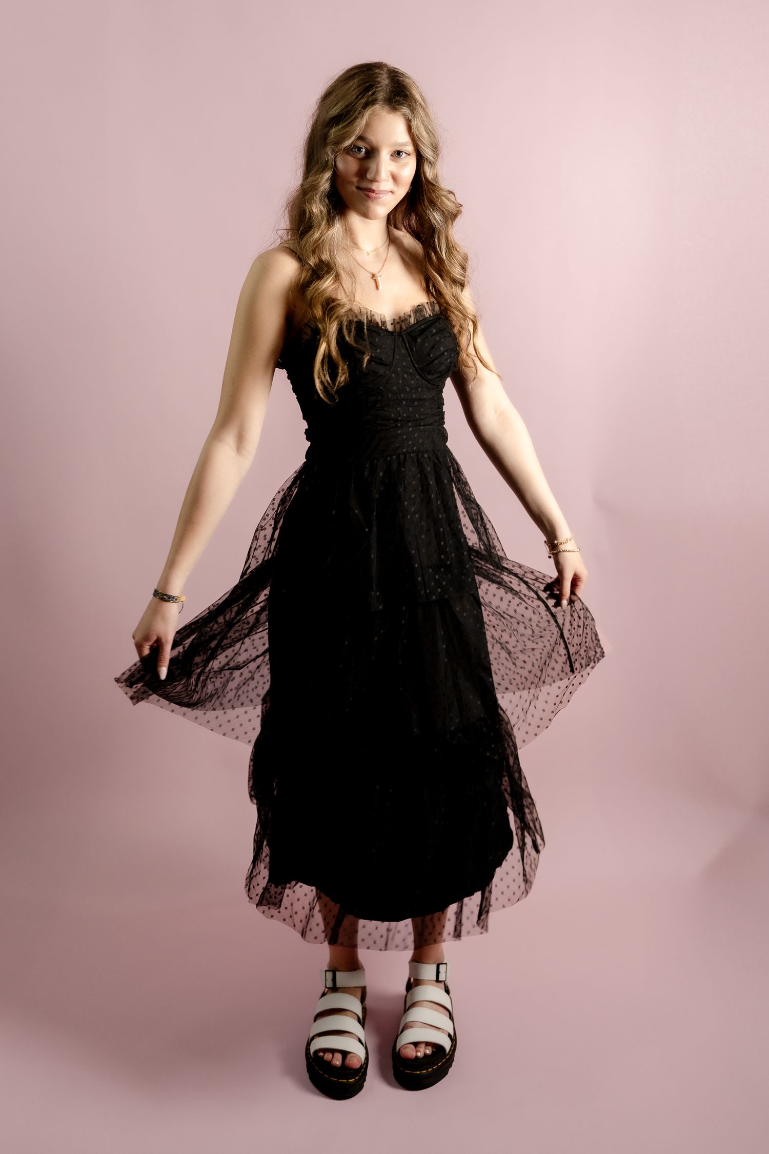 A black lace dress is shown in dynamic movement against a pink studio background.
