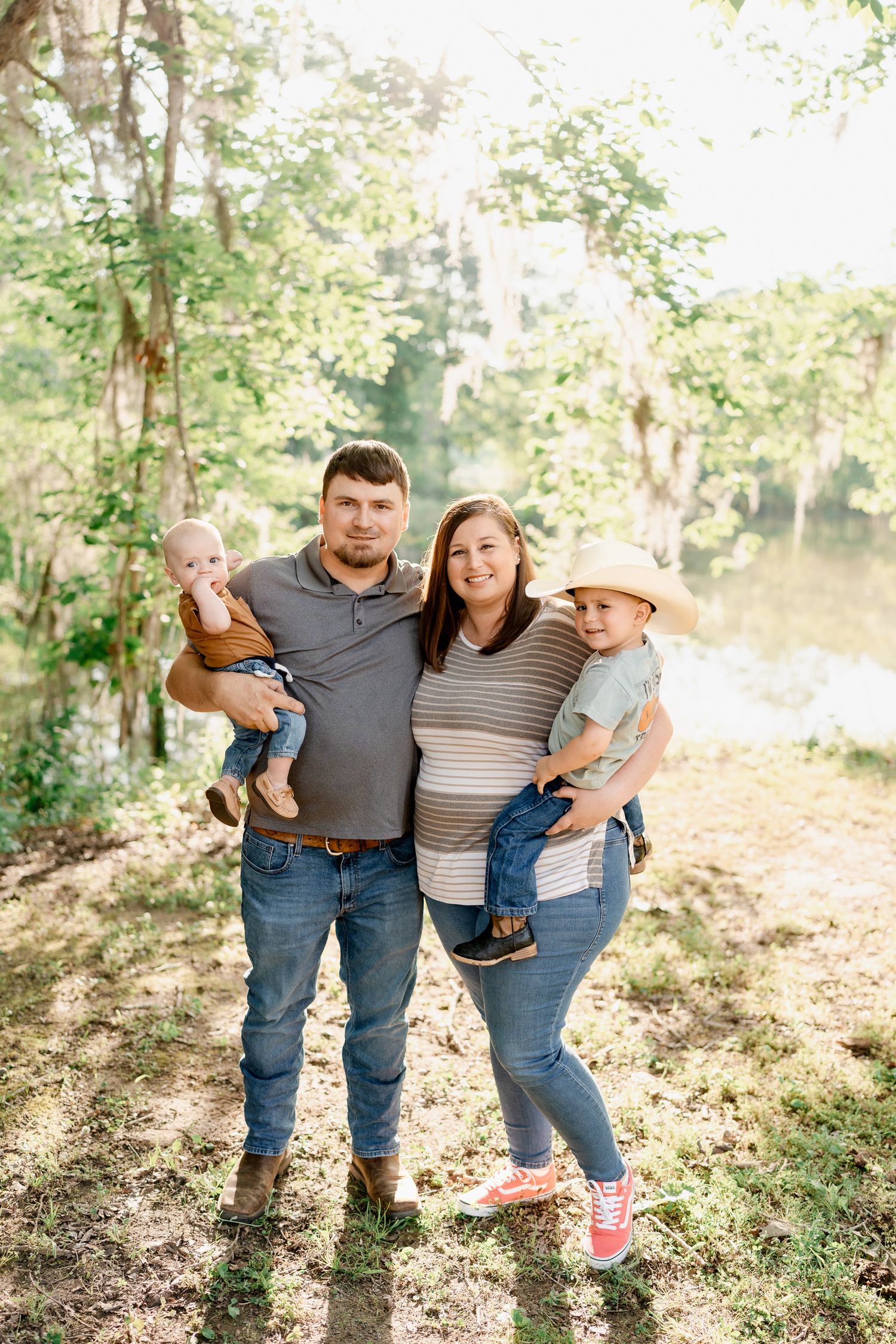 Family in casual denim poses together during an outdoor photo session near water.