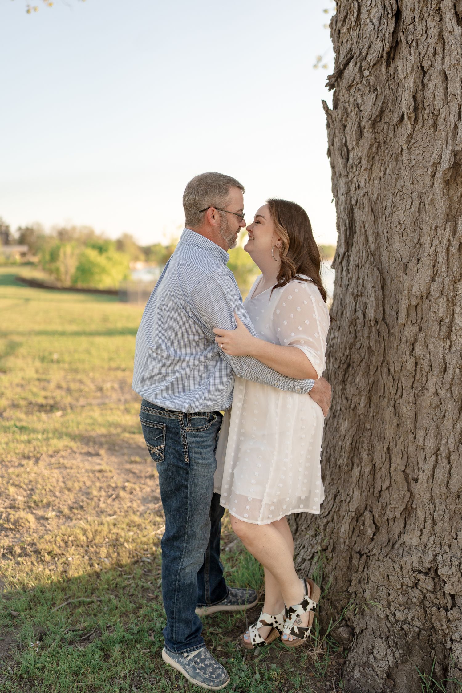 A tender moment shared between a couple against a large tree trunk.