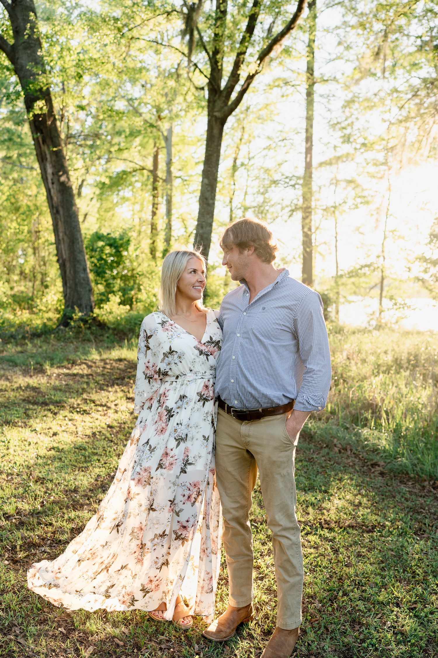 A couple shares a joyful moment in golden afternoon light among tall trees.