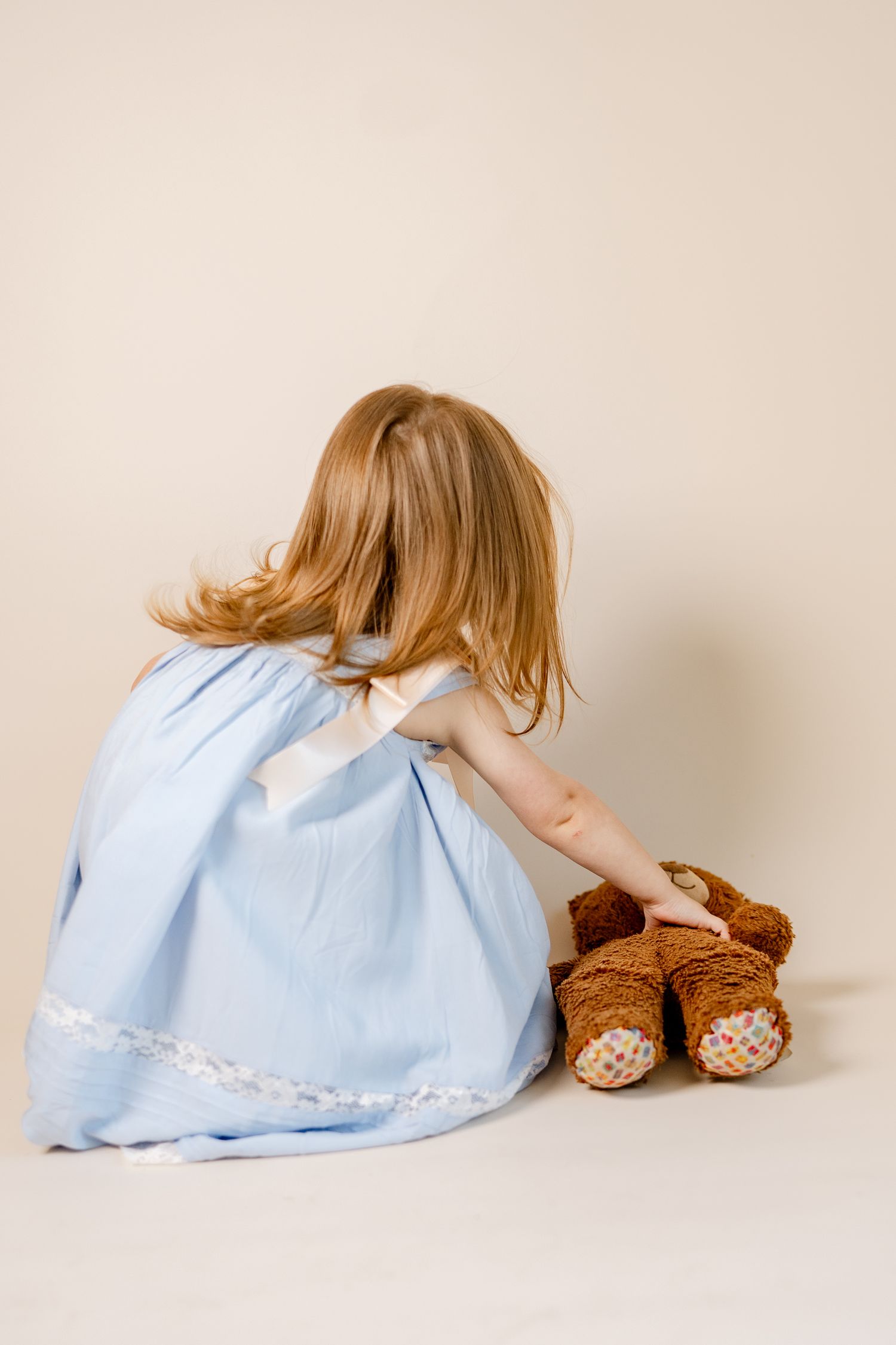 A brown teddy bear companions a light blue dress in an artistic studio composition.