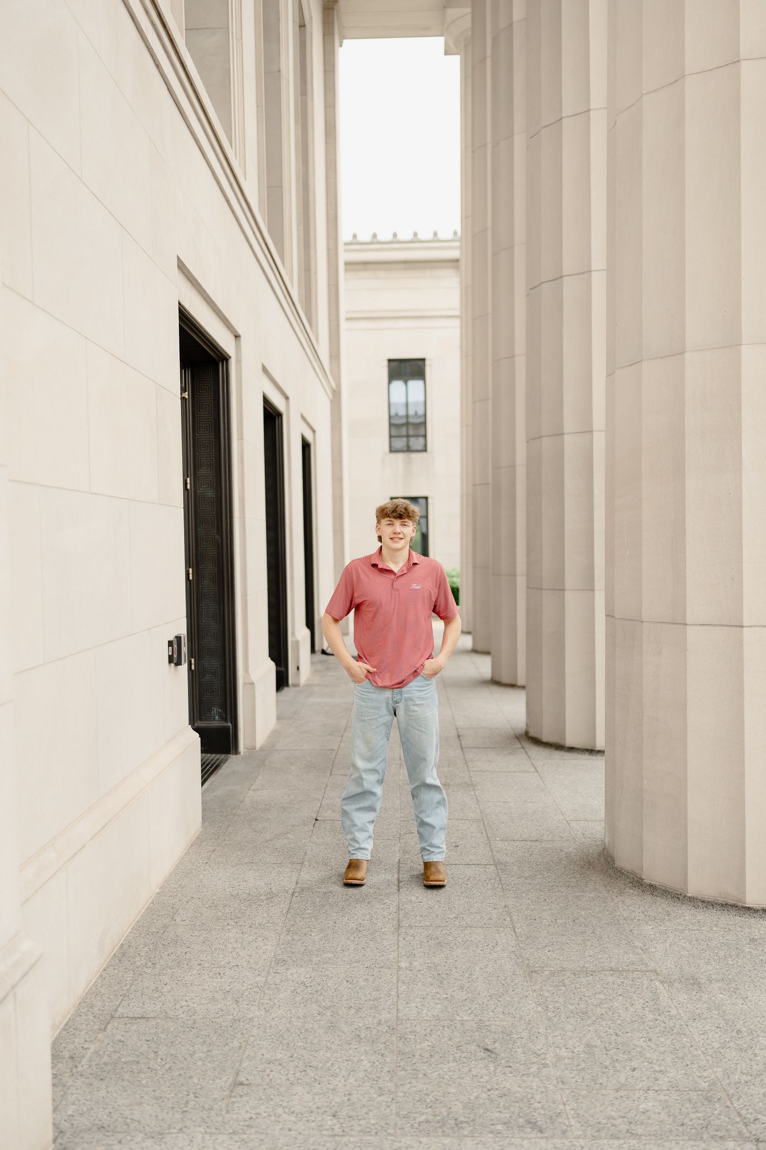 Standing portrait in hallway between classical white columns and black doors.