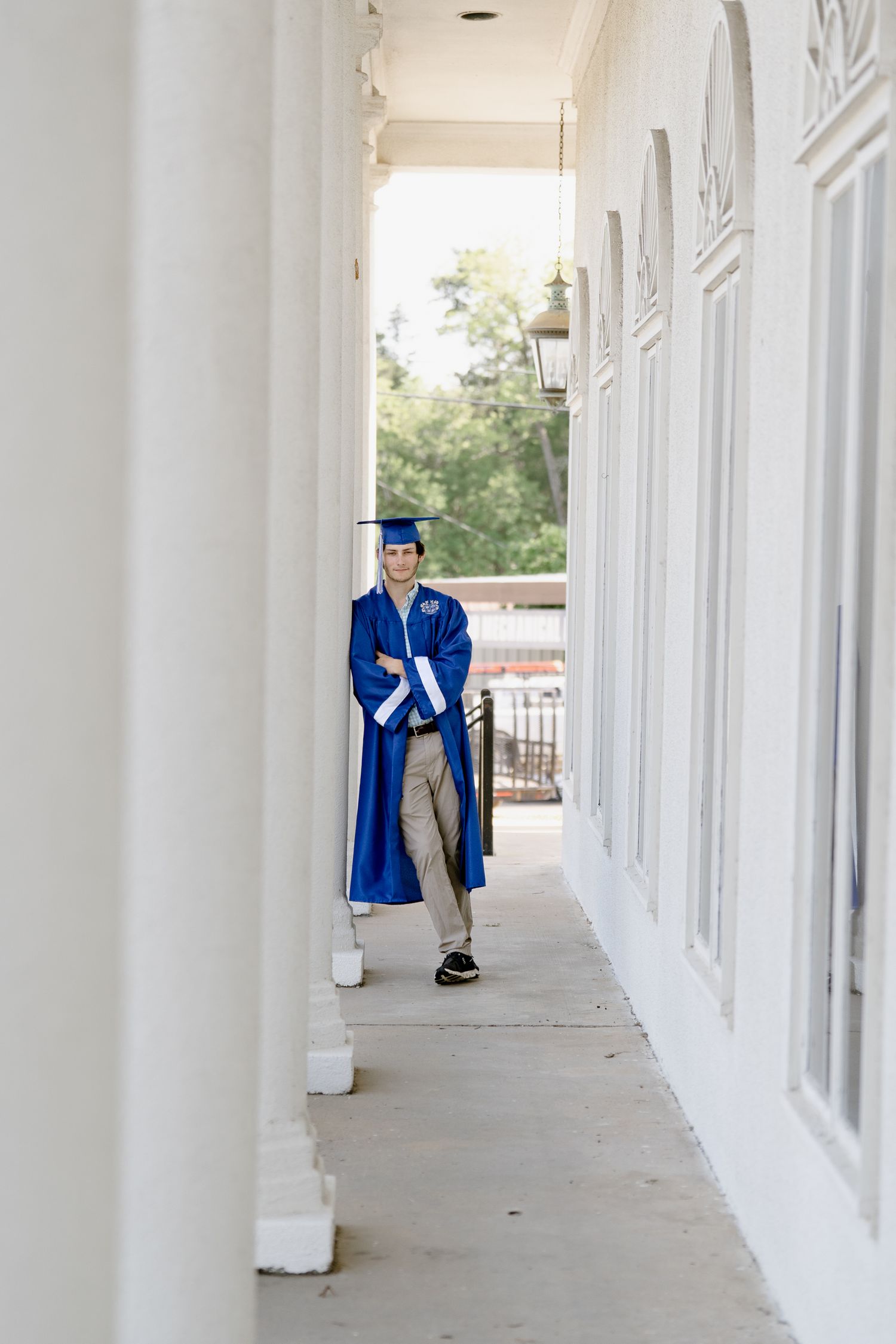 Graduate poses in blue academic regalia against white pillared walkway.