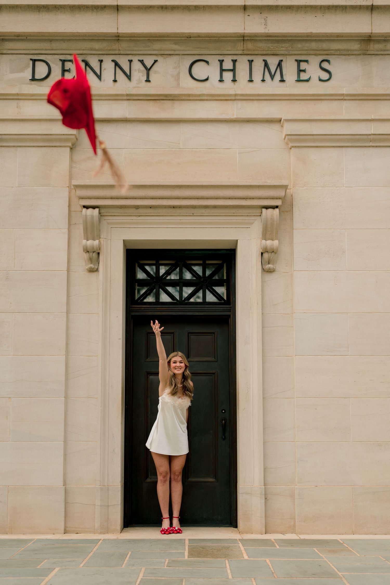 A sequence showing a person in a white dress throwing a red graduation cap in front of the Denny Chimes building.
