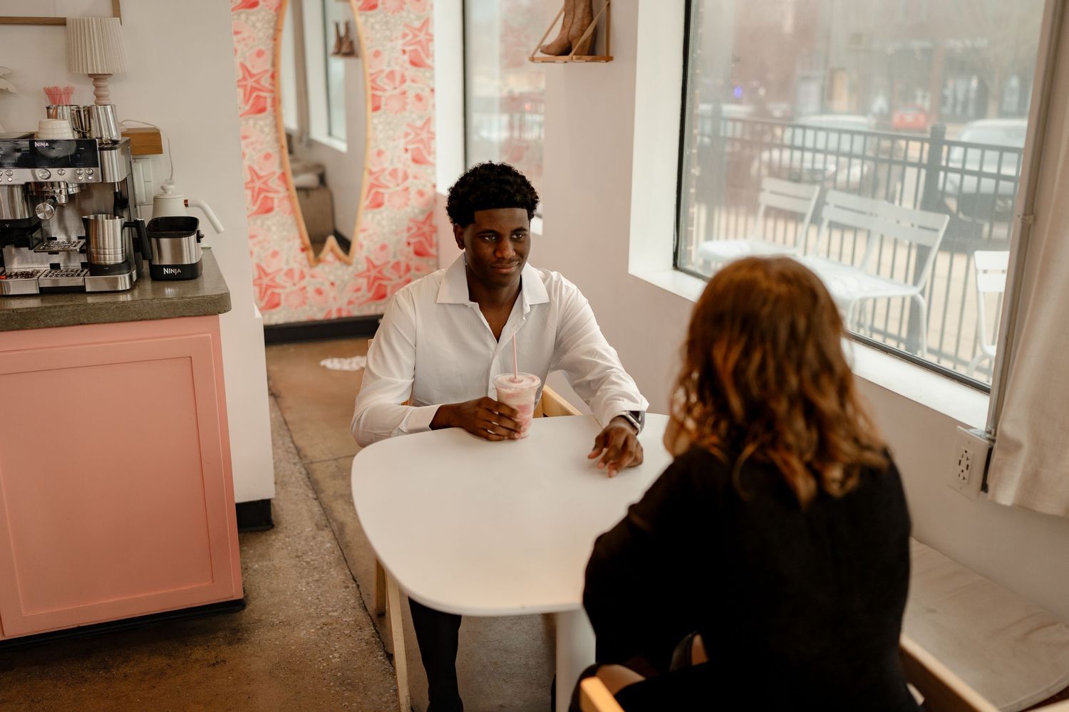 Interracial couple sharing a romantic coffee date inside a charming pink cafe interior.