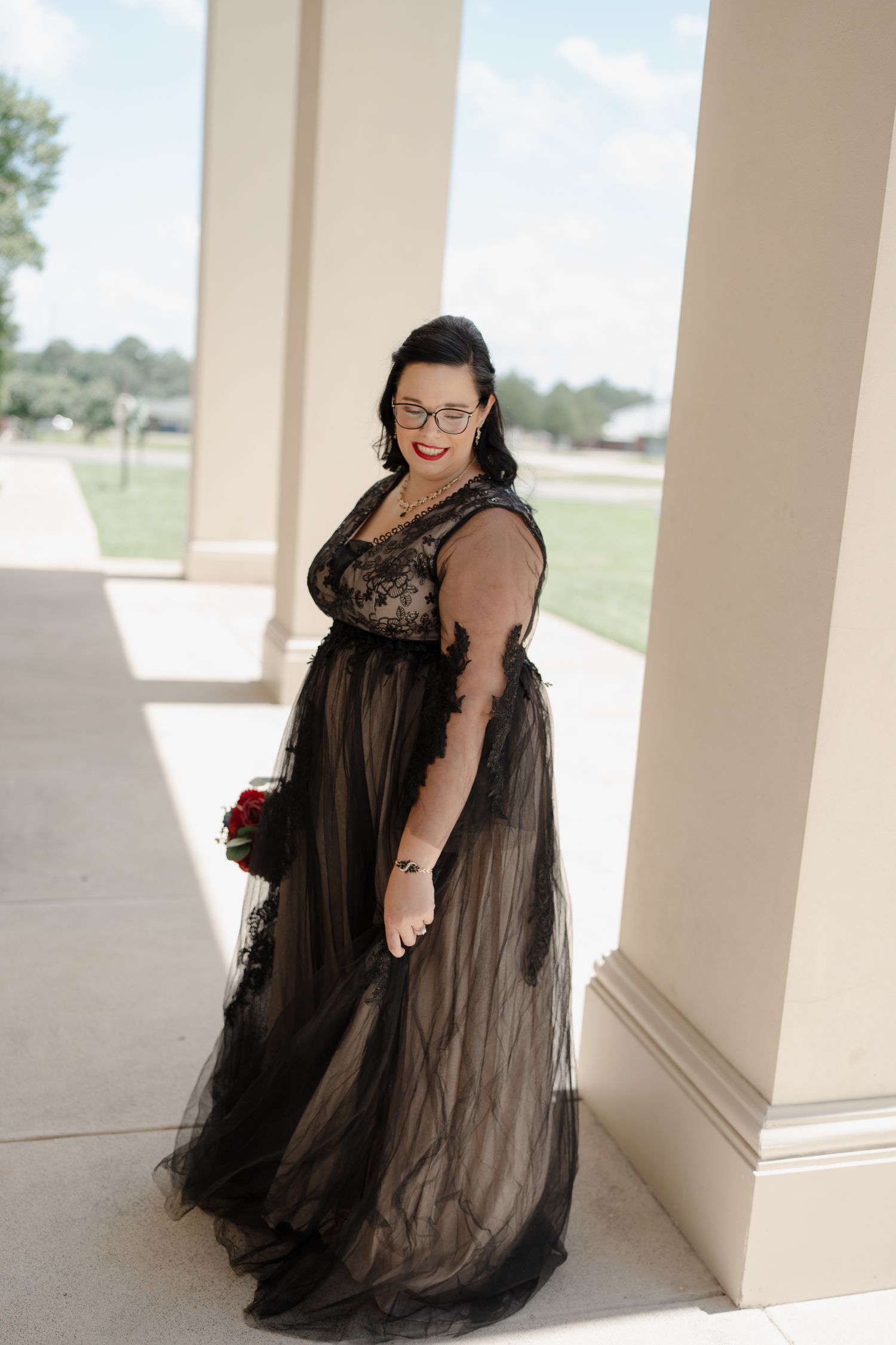 Elegant black tulle evening gown photographed against cream pillars outdoors.