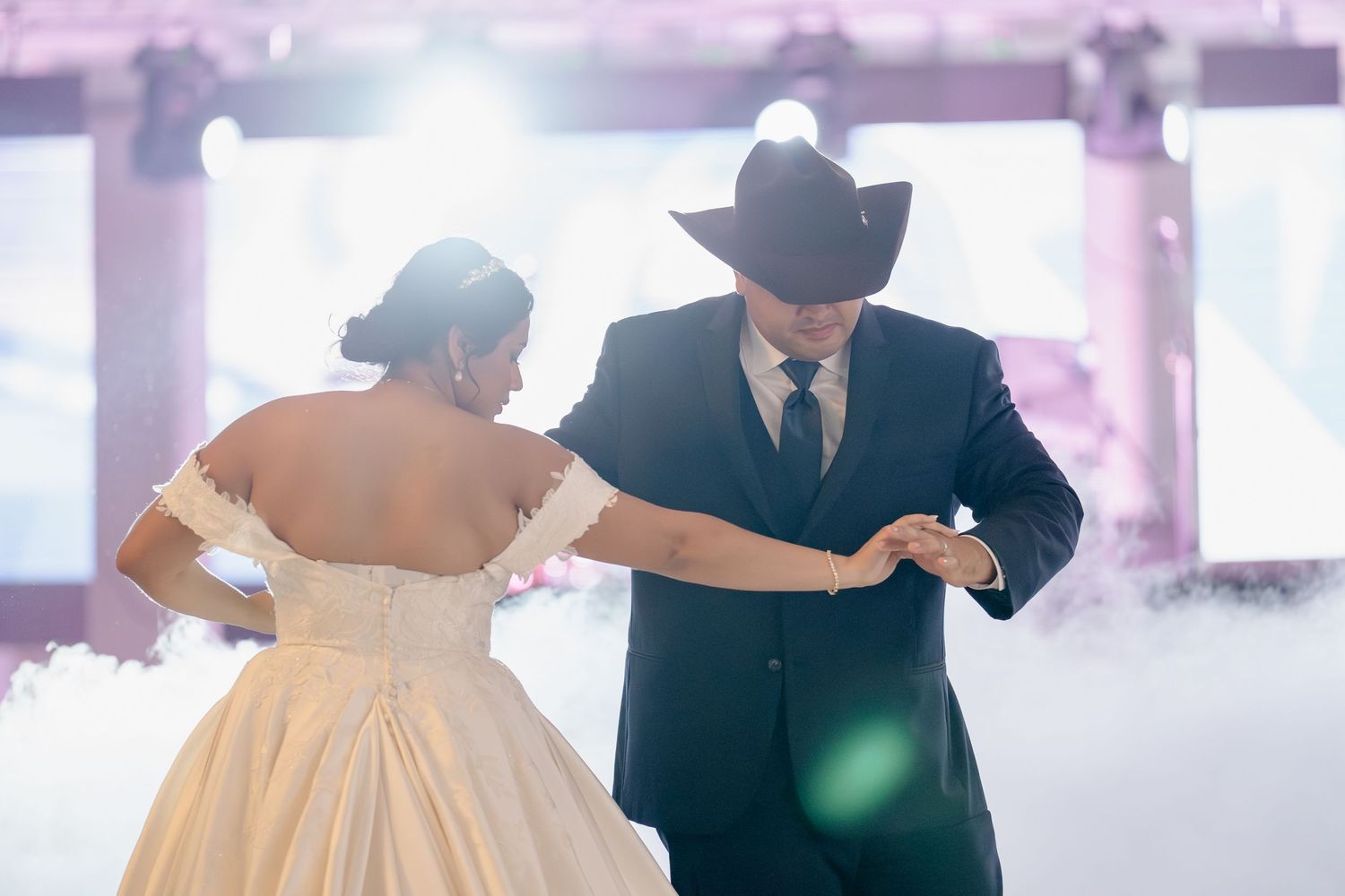 A bride in a flowing champagne-colored ballgown dances with a groom in a black tuxedo at an elegant wedding reception.