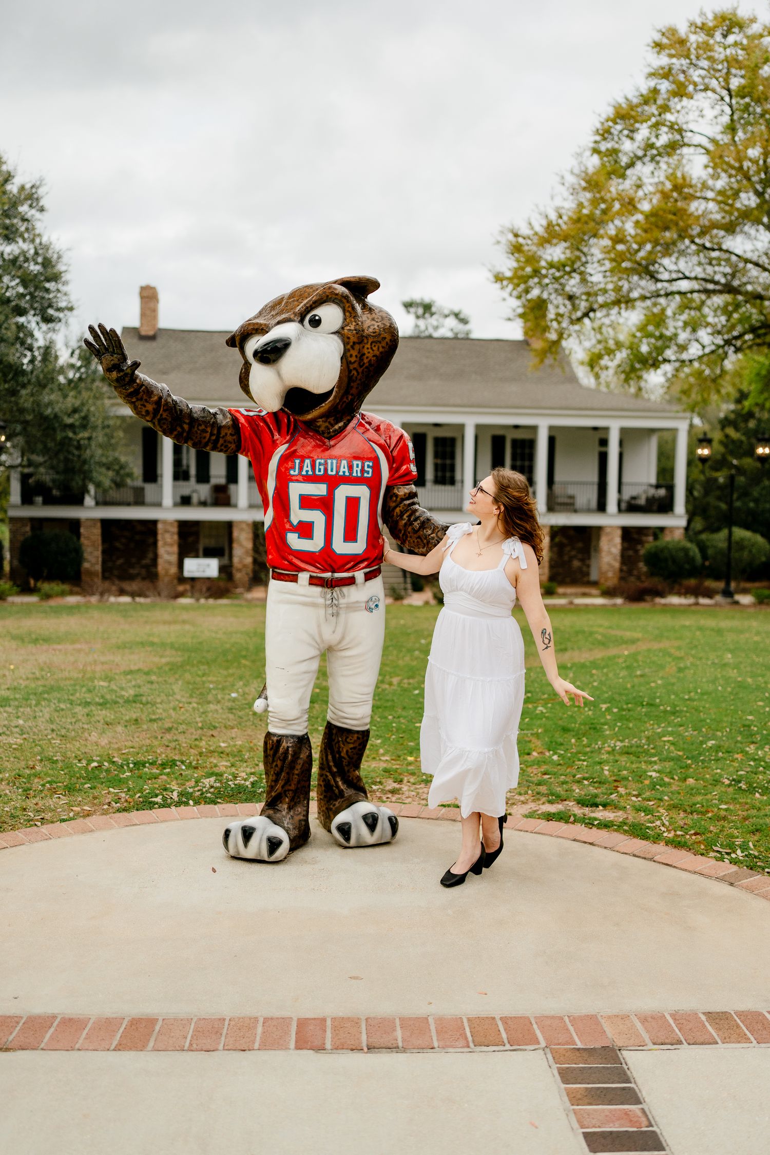 Graduate poses with university mascot wearing jersey number 50 on campus lawn.
