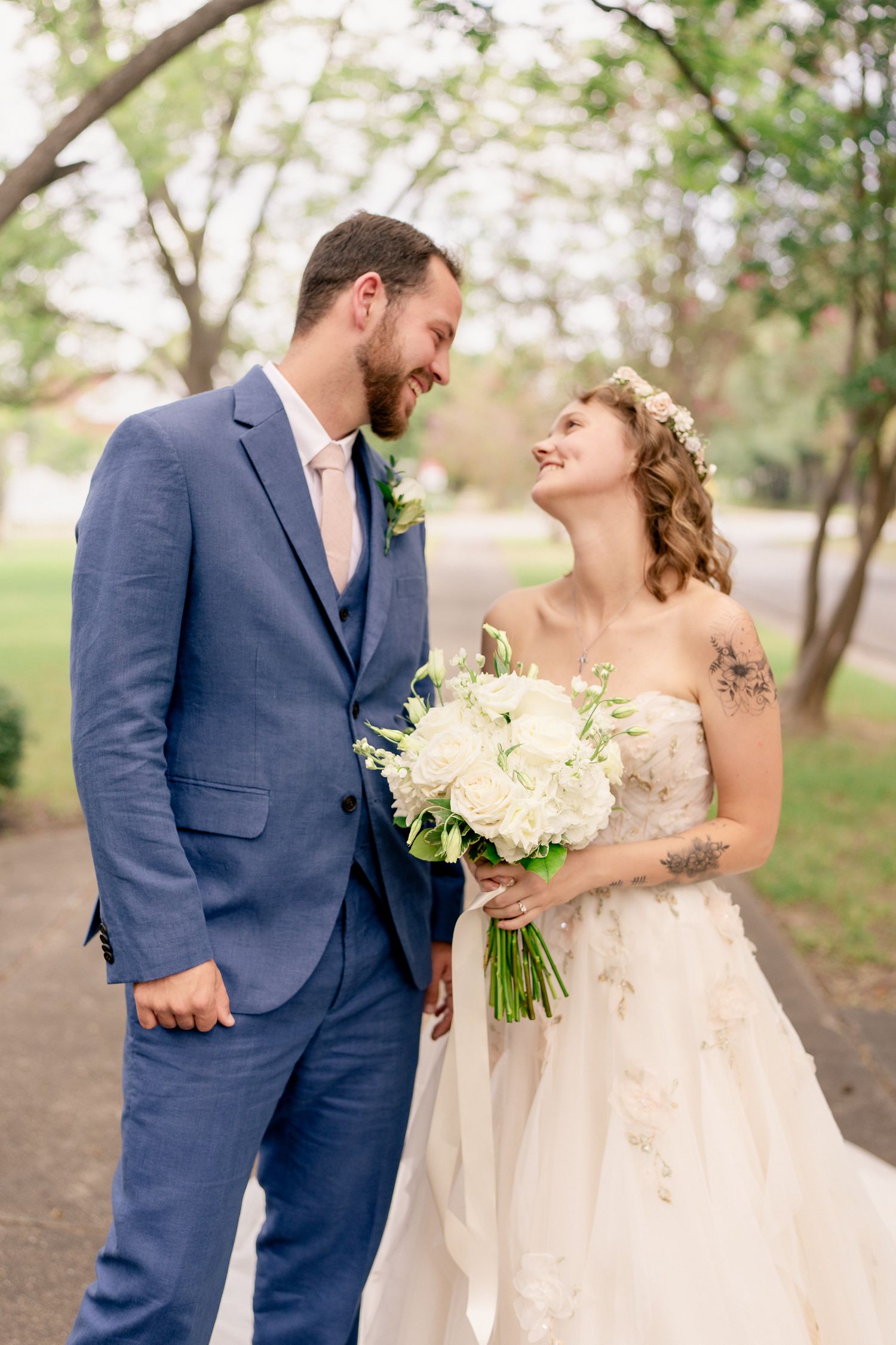 A romantic wedding couple shares joyful moments in a natural outdoor setting wearing navy blue suit and white gown.