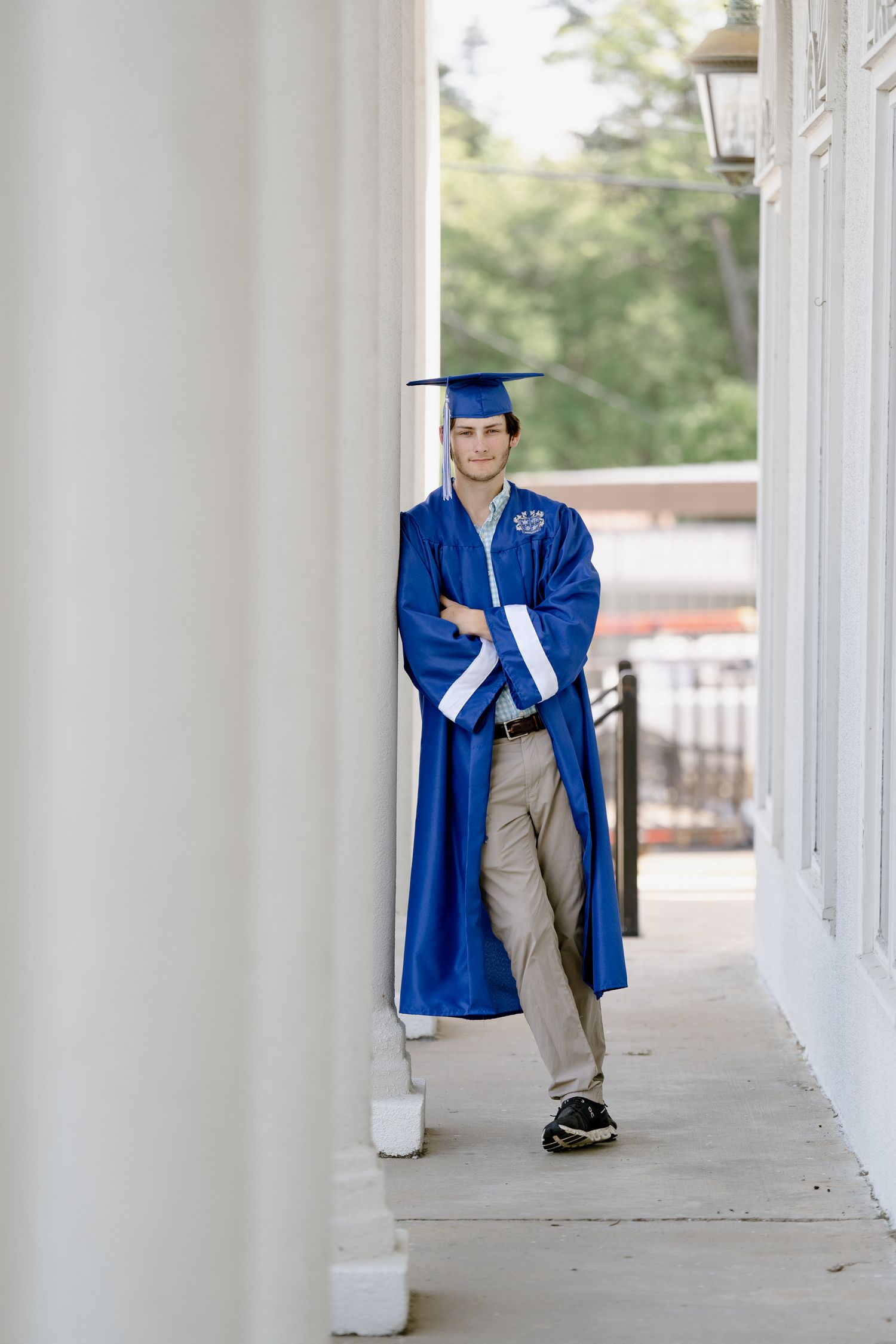 Graduate in royal blue gown walks confidently through classical columned hallway.
