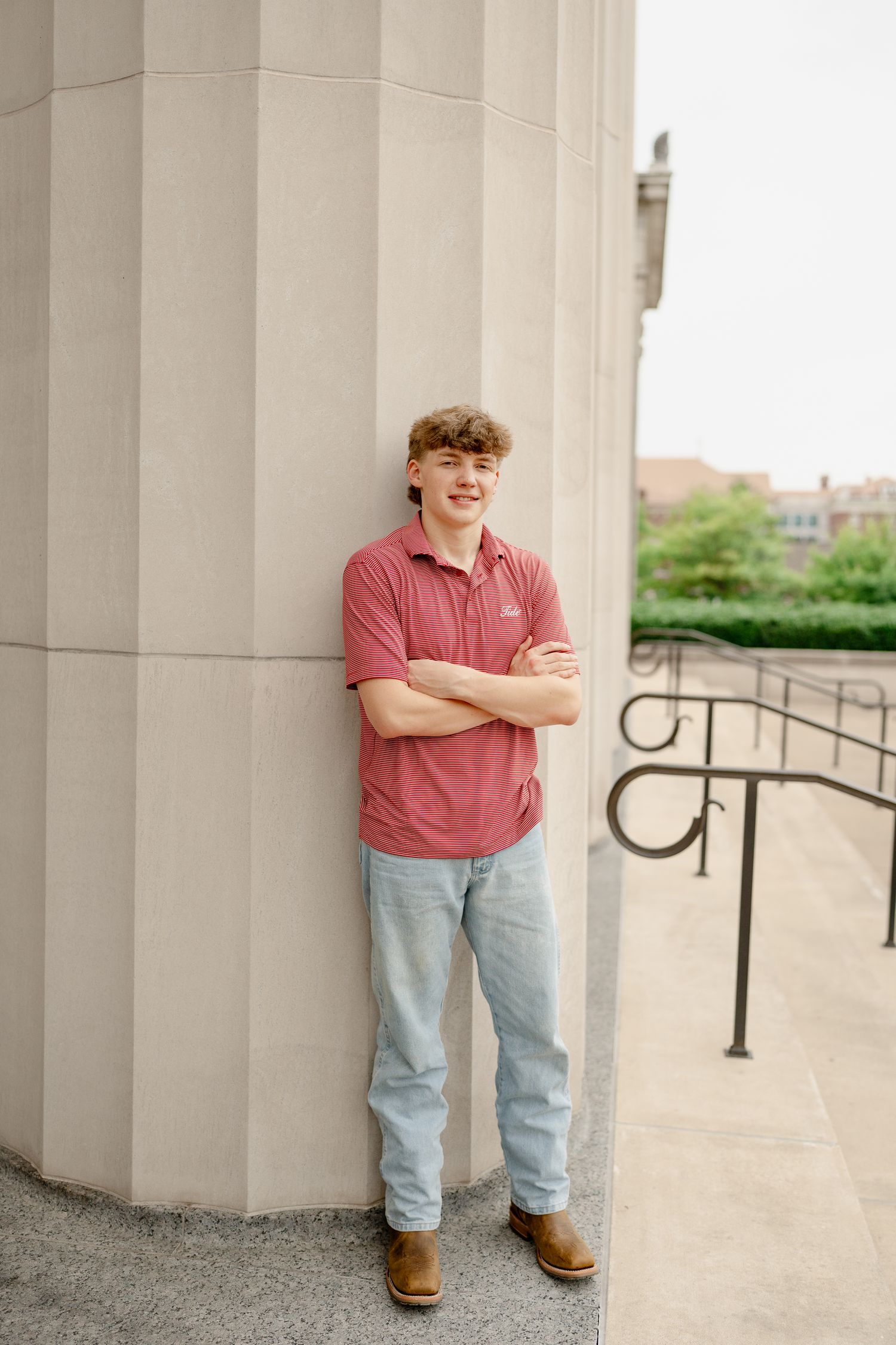 Casual pose against cream colored building column with arms crossed.