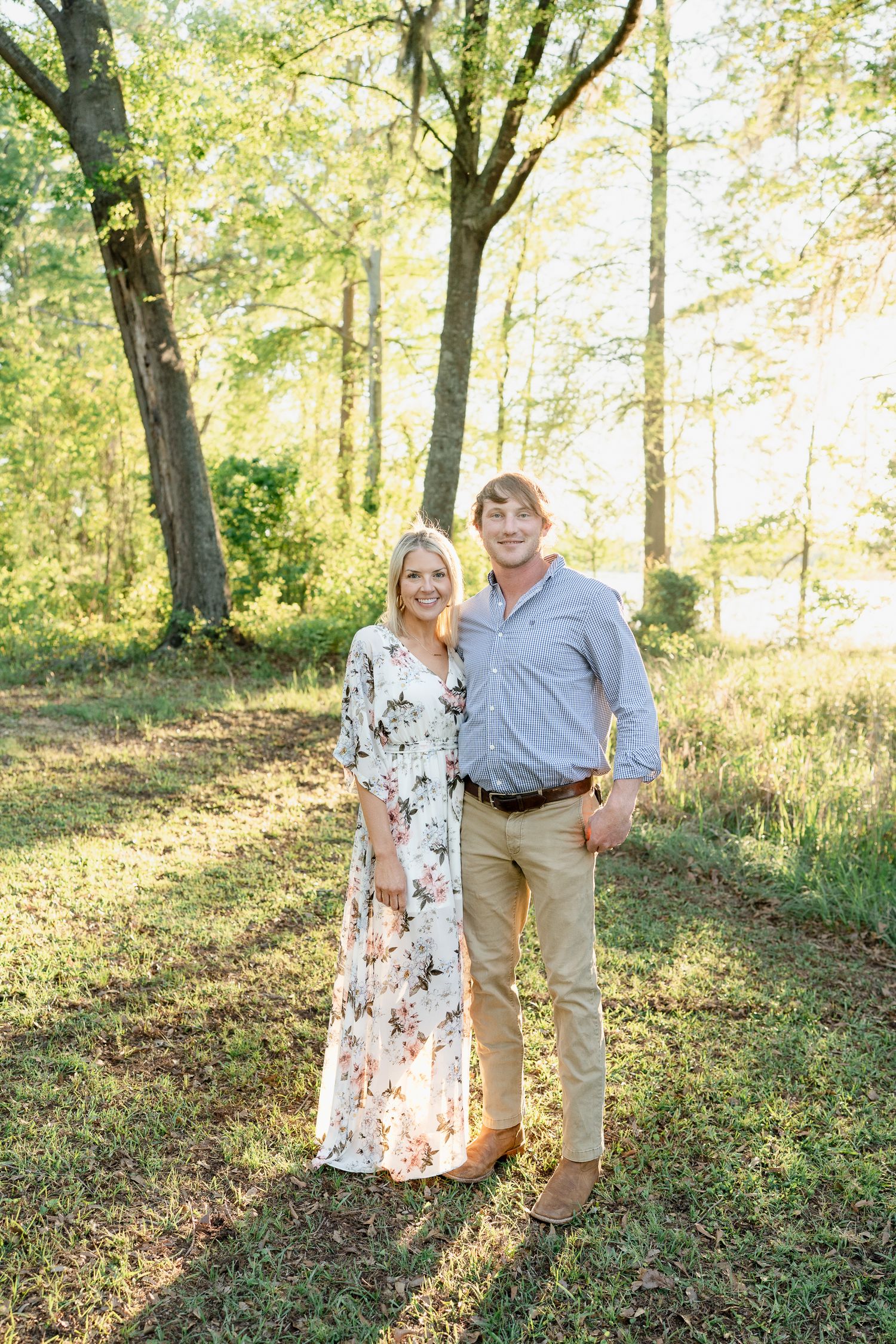 A couple poses together in a sun-dappled forest clearing.