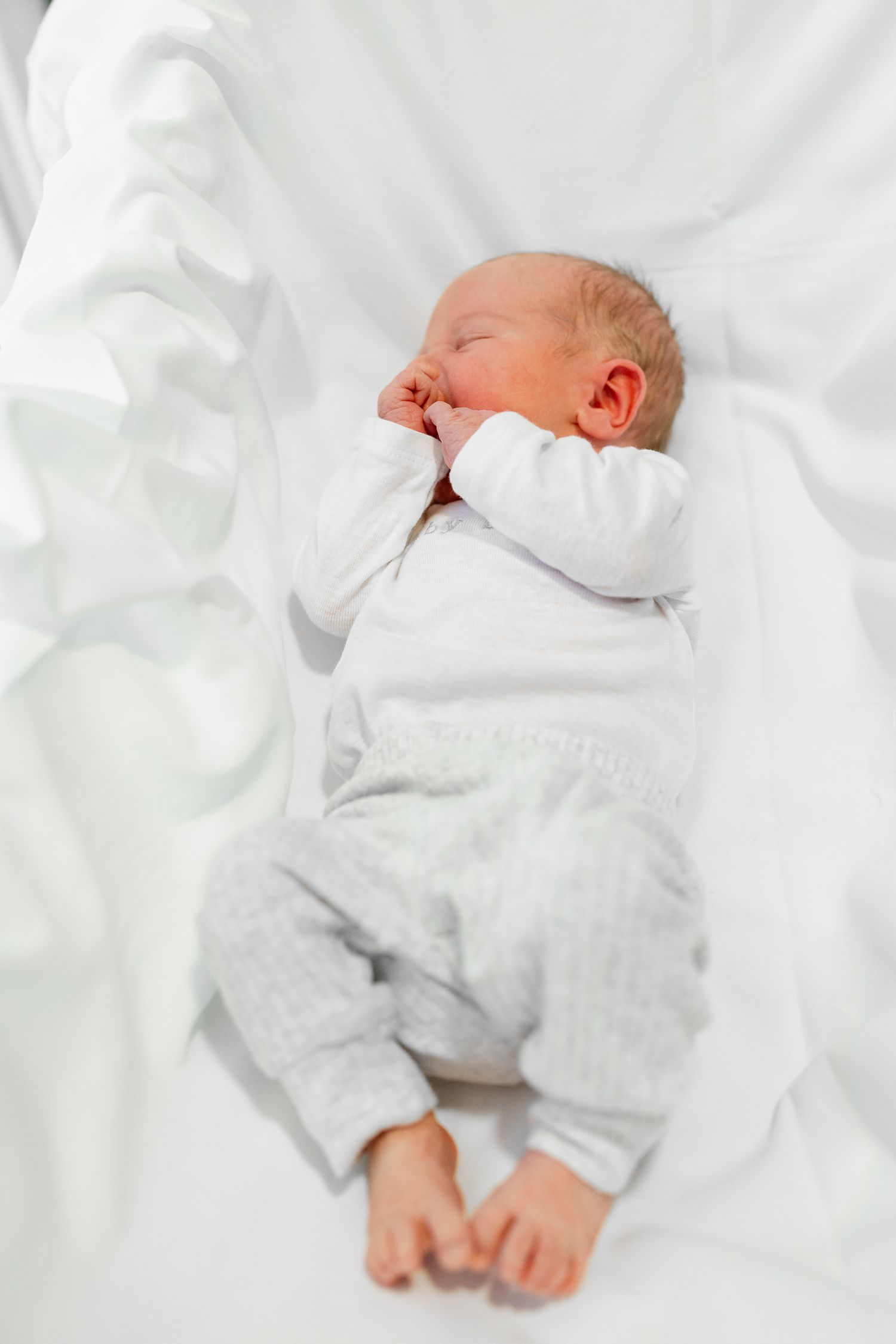 Sleeping newborn in soft white clothing nestled in white bedding.
