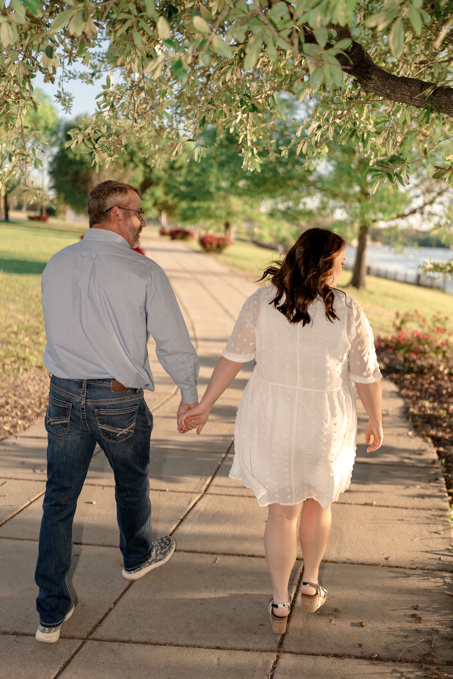 A couple walking together on a tree-lined pathway during golden hour.