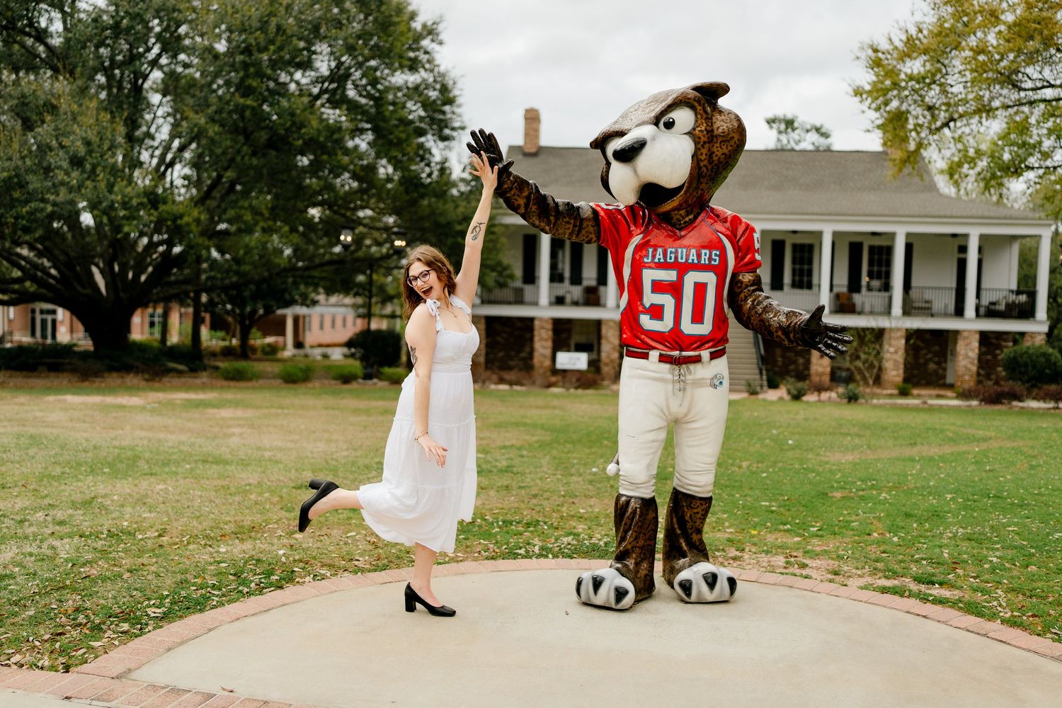 Graduate walks towards mascot on campus sidewalk during graduation photo session.
