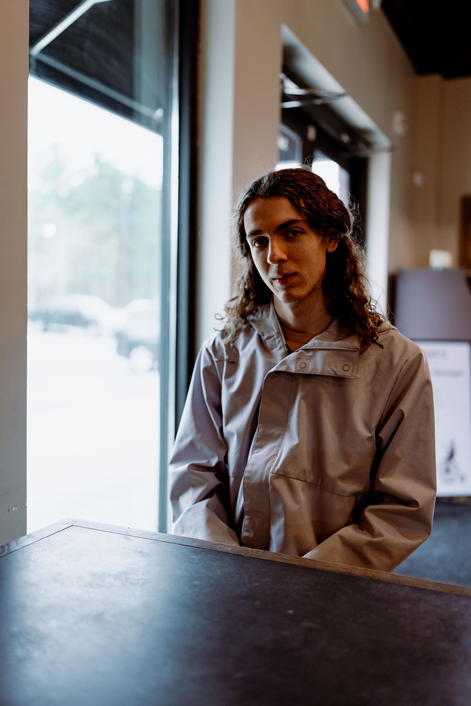 Moody indoor portraits by large windows in a white button-up shirt.