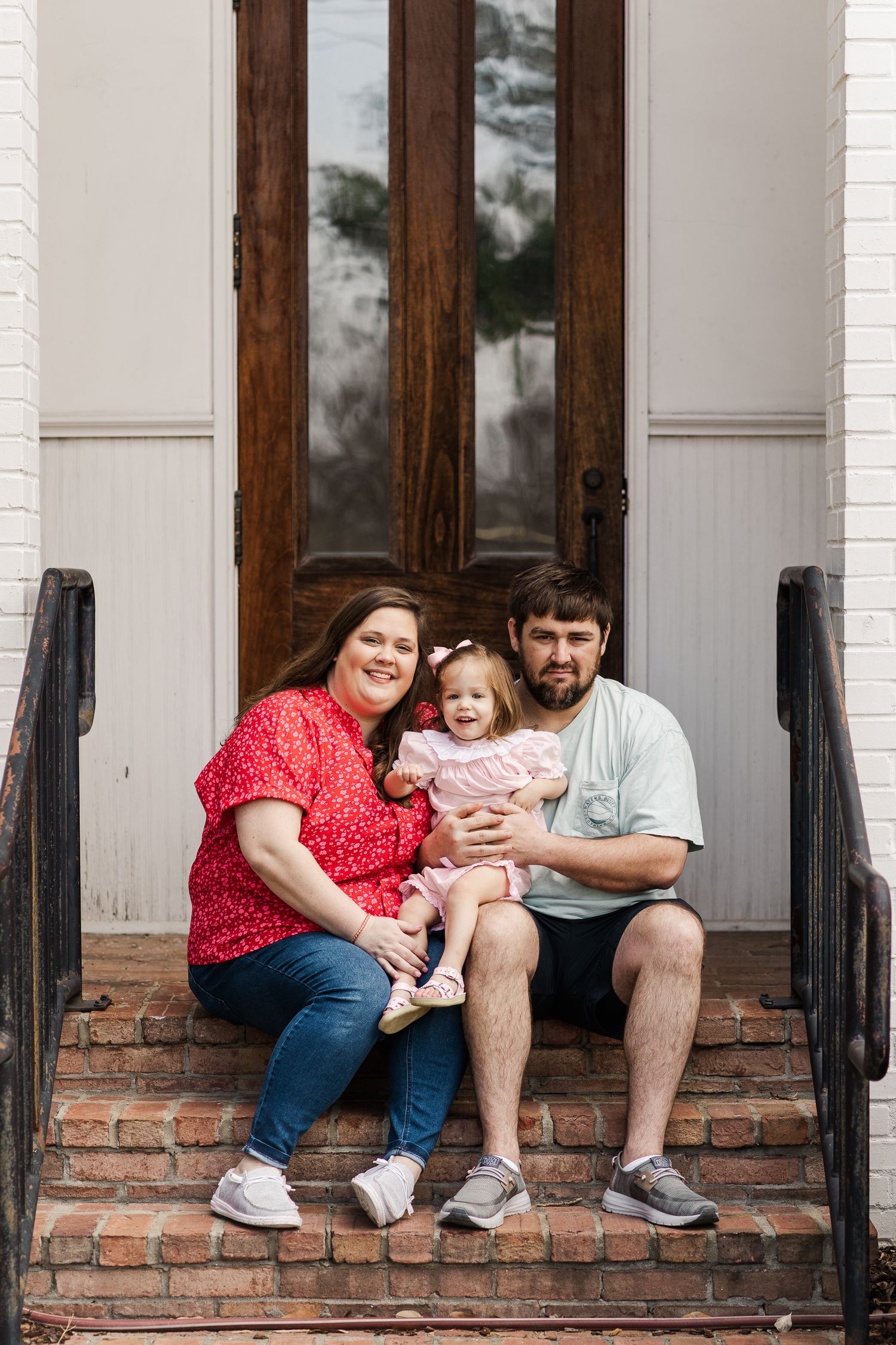 Family sitting together on brick steps in front of wooden door.