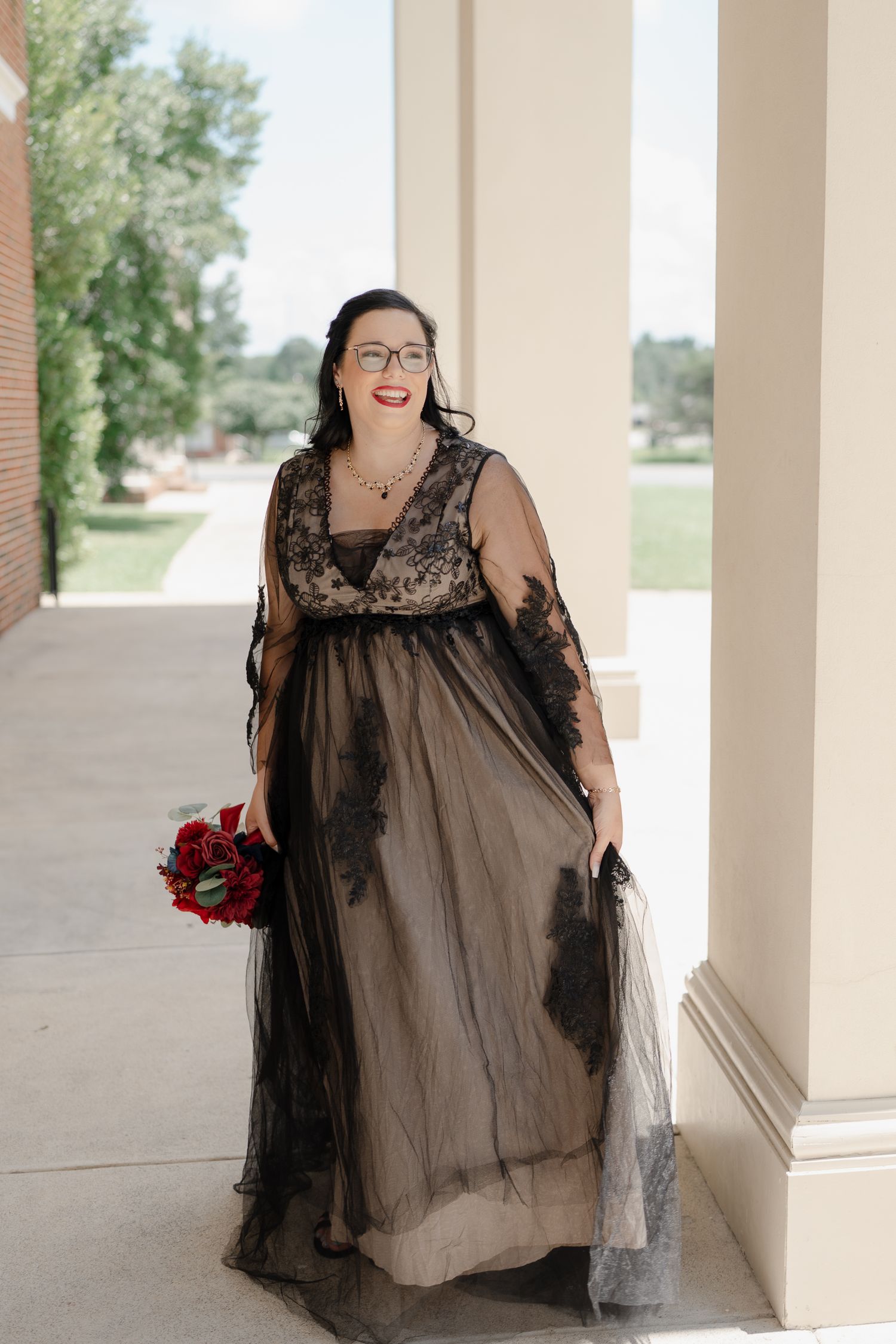 Black lace formal dress photographed in an outdoor colonnade setting.