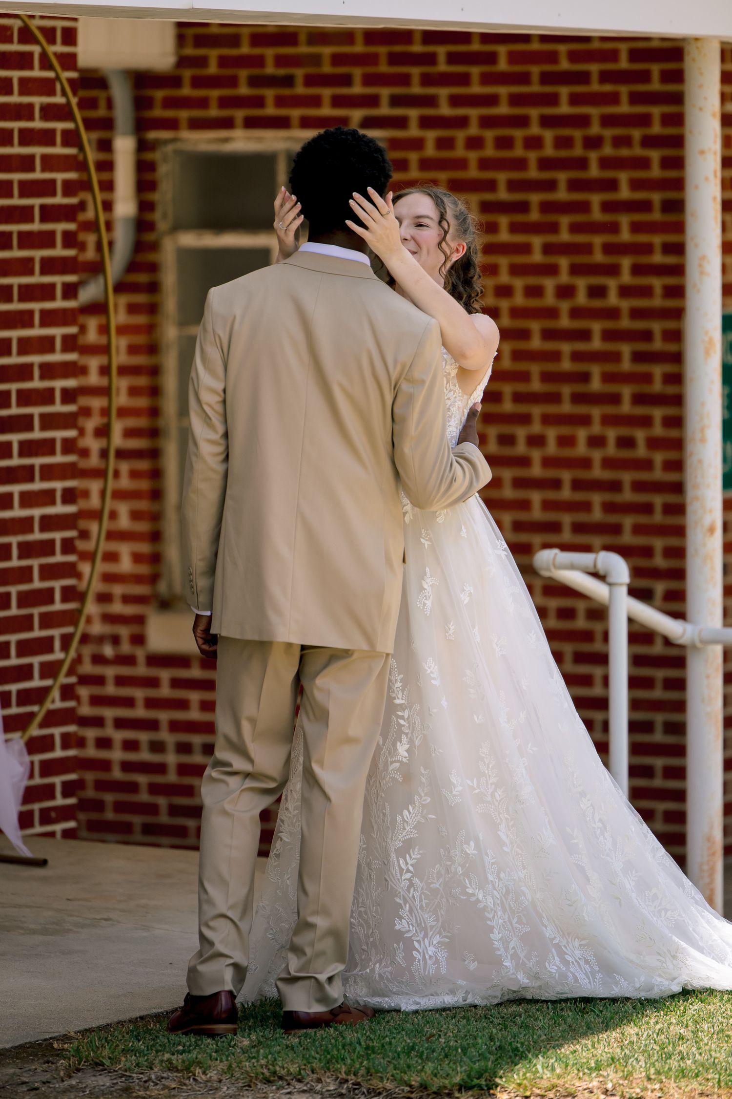 Bride and groom share first kiss in front of brick church during outdoor wedding ceremony.