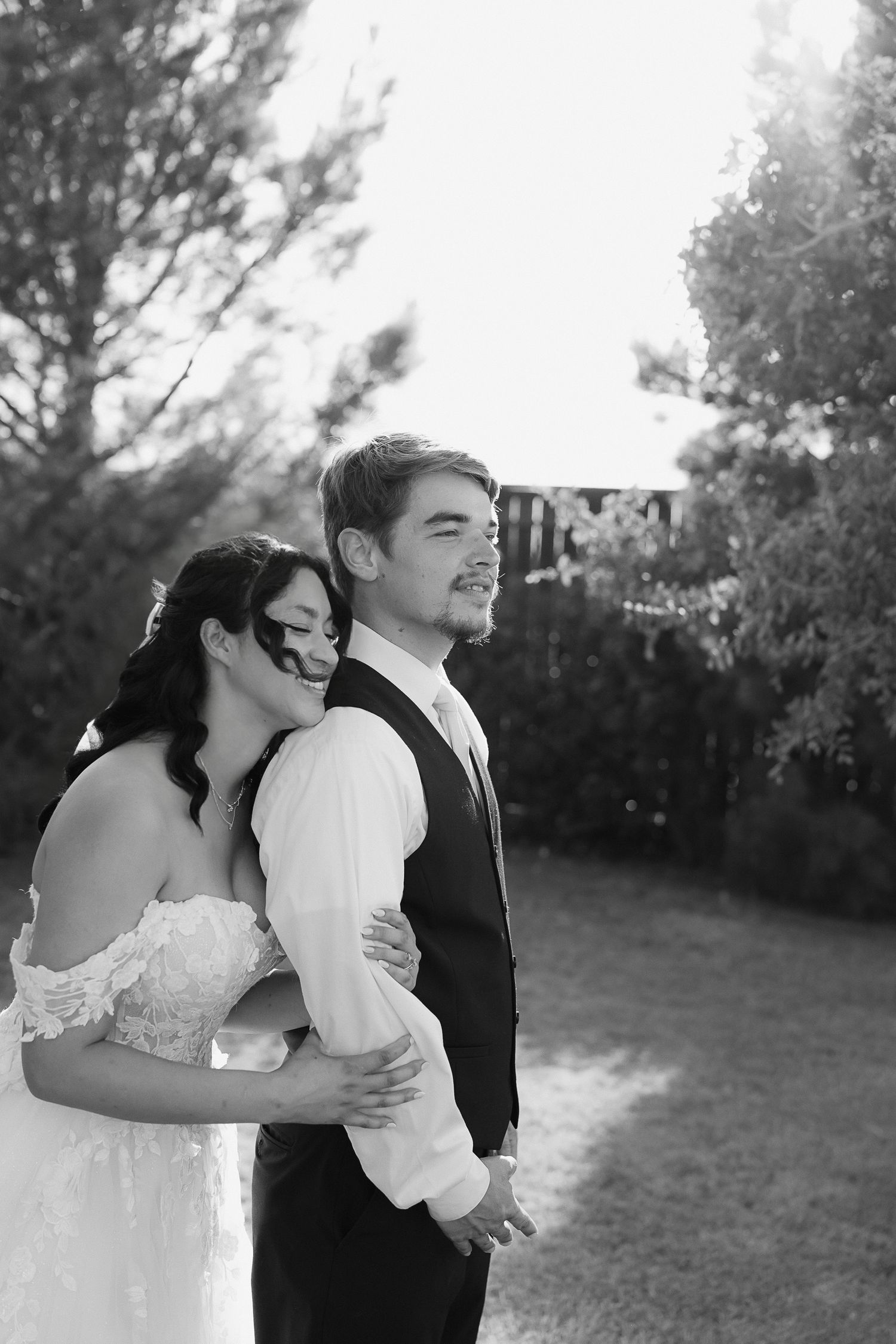 Black and white portrait of bride and groom embracing tenderly in garden setting.