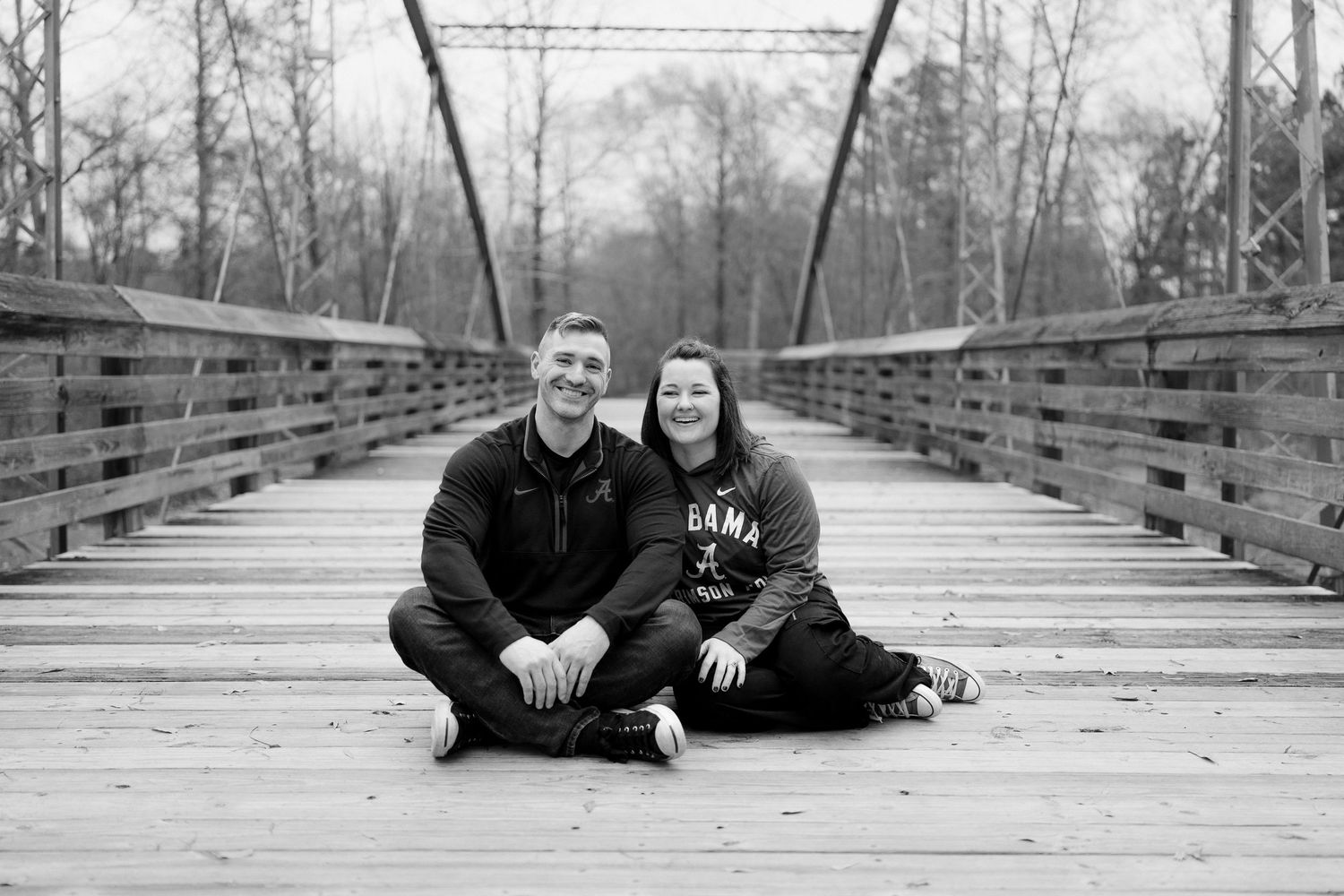 A couple sits together on a wooden bridge deck in black and white photography.