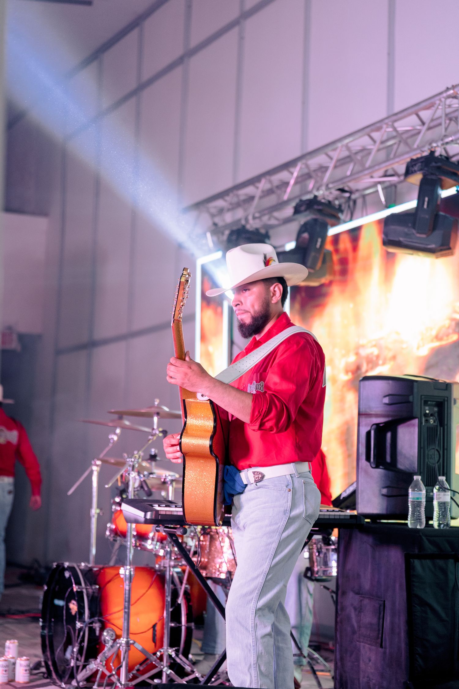 A musician in red performs with a guitar on stage at an indoor event.