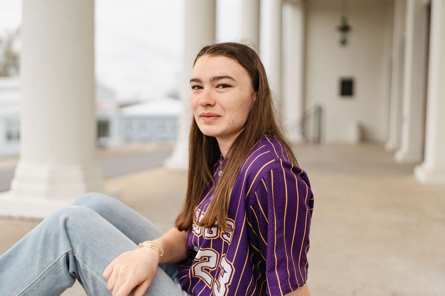 Casual poses against white columns in vintage-style baseball uniform and denim.