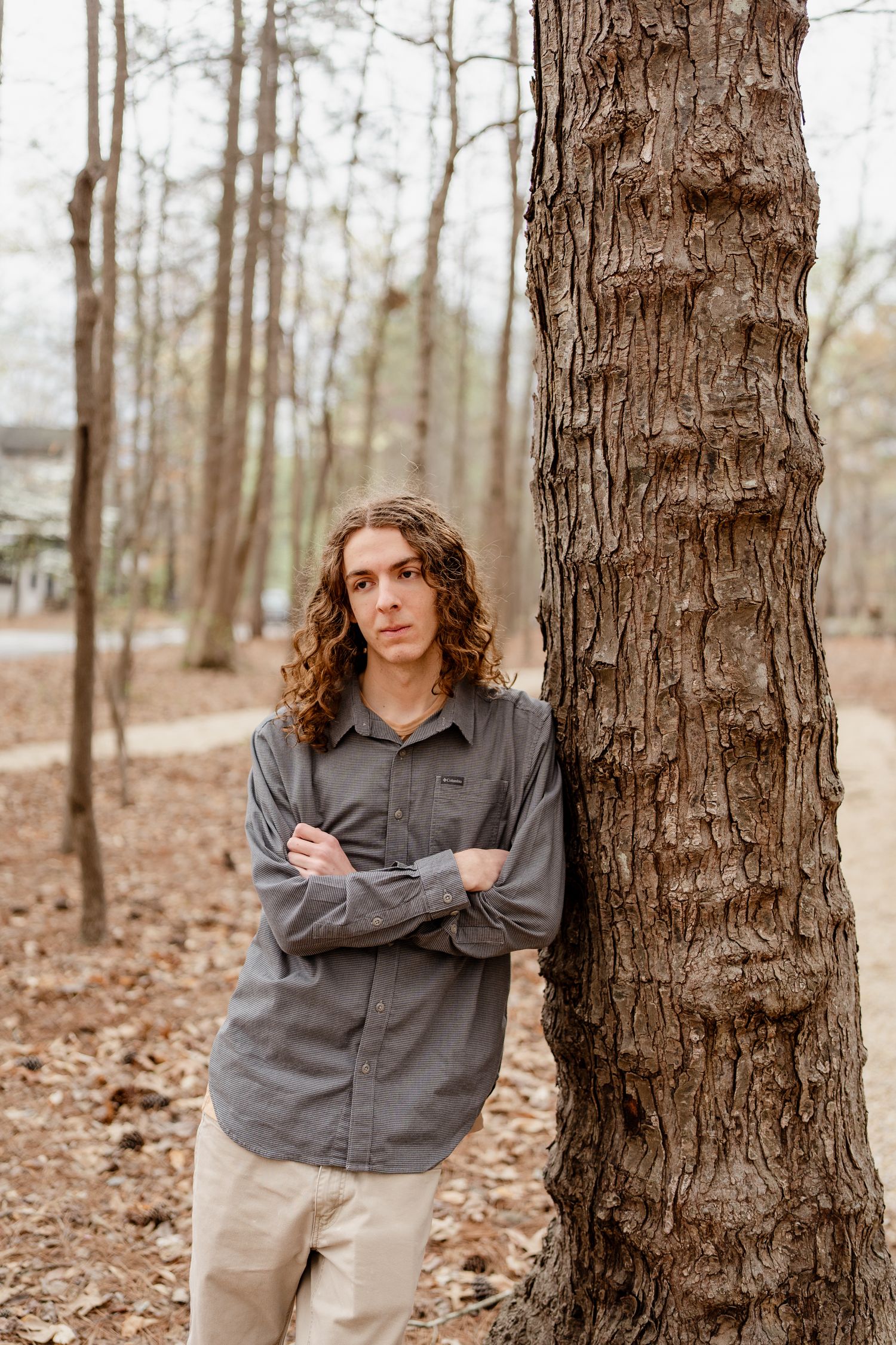 Person in gray button-up shirt posed between trees with arms crossed.