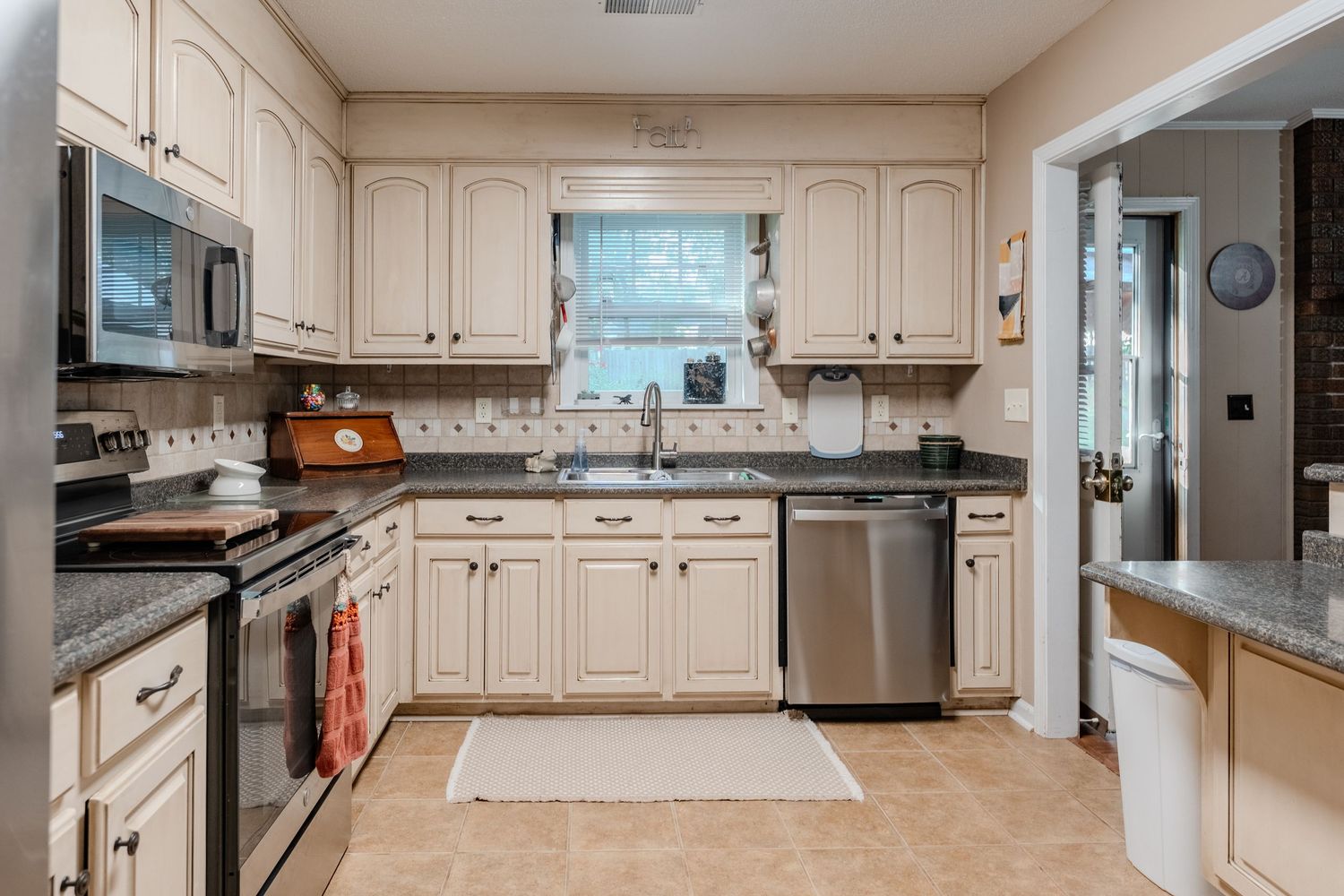 Modern kitchen with cream-colored cabinets, stainless steel appliances, and granite countertops in a U-shaped layout.