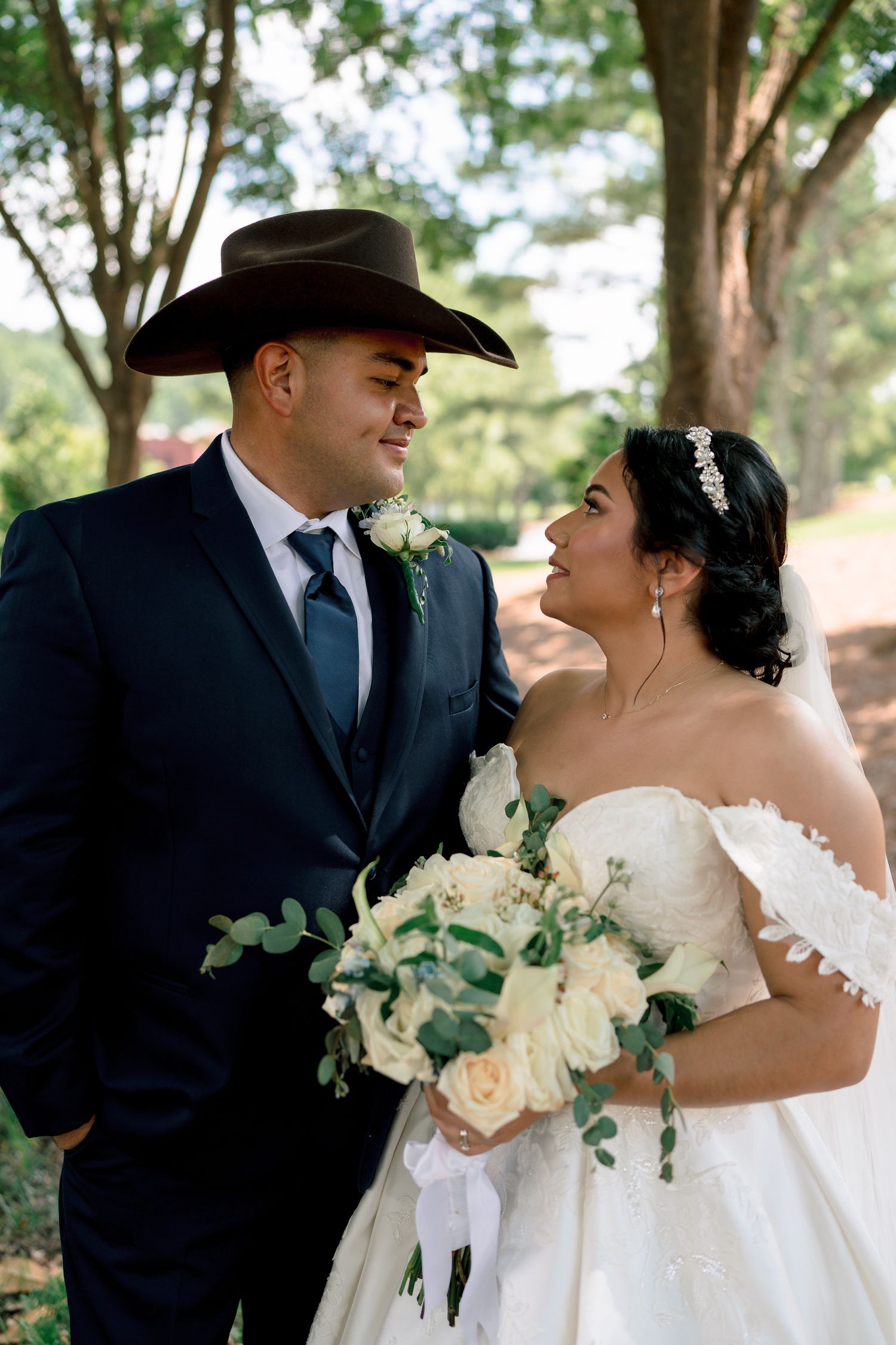 A romantic wedding couple shares intimate moments in a garden setting with the groom wearing a black cowboy hat.