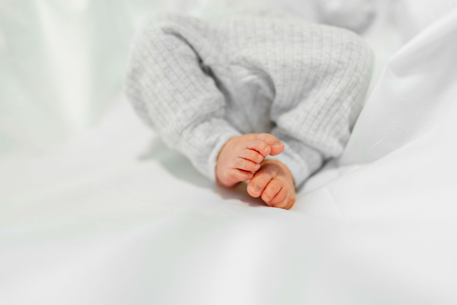 Close up of tiny baby hand in gray sweater against white bedding.