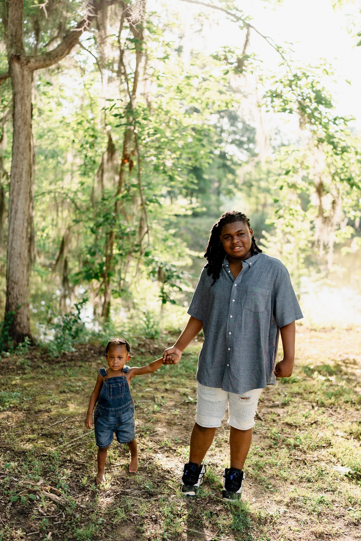 Parent and child walking and playing together through a sunny wooded area in coordinated outfits.