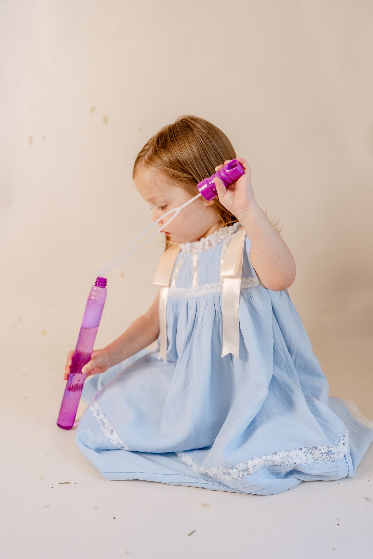 A purple bubble wand and light blue dress create a whimsical scene on a white floor.