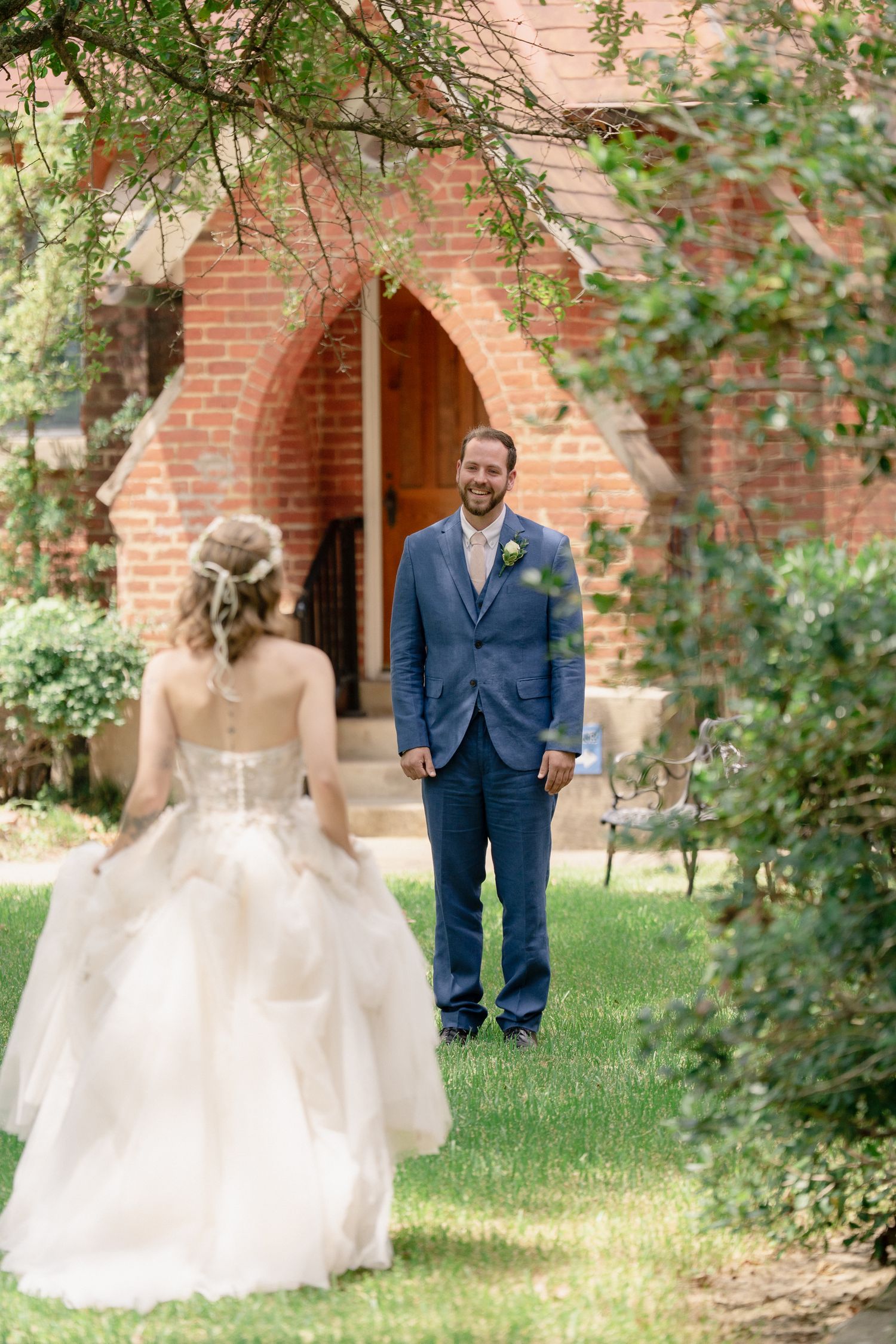 A couple shares their first look moment in a garden setting with brick archways and lush greenery.