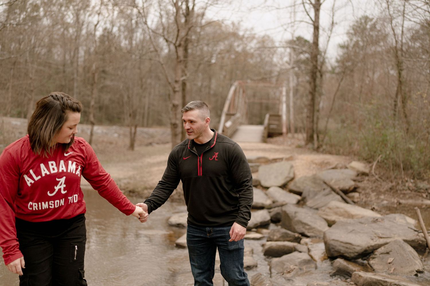 Two people walk hand in hand along a rocky path in a natural setting.