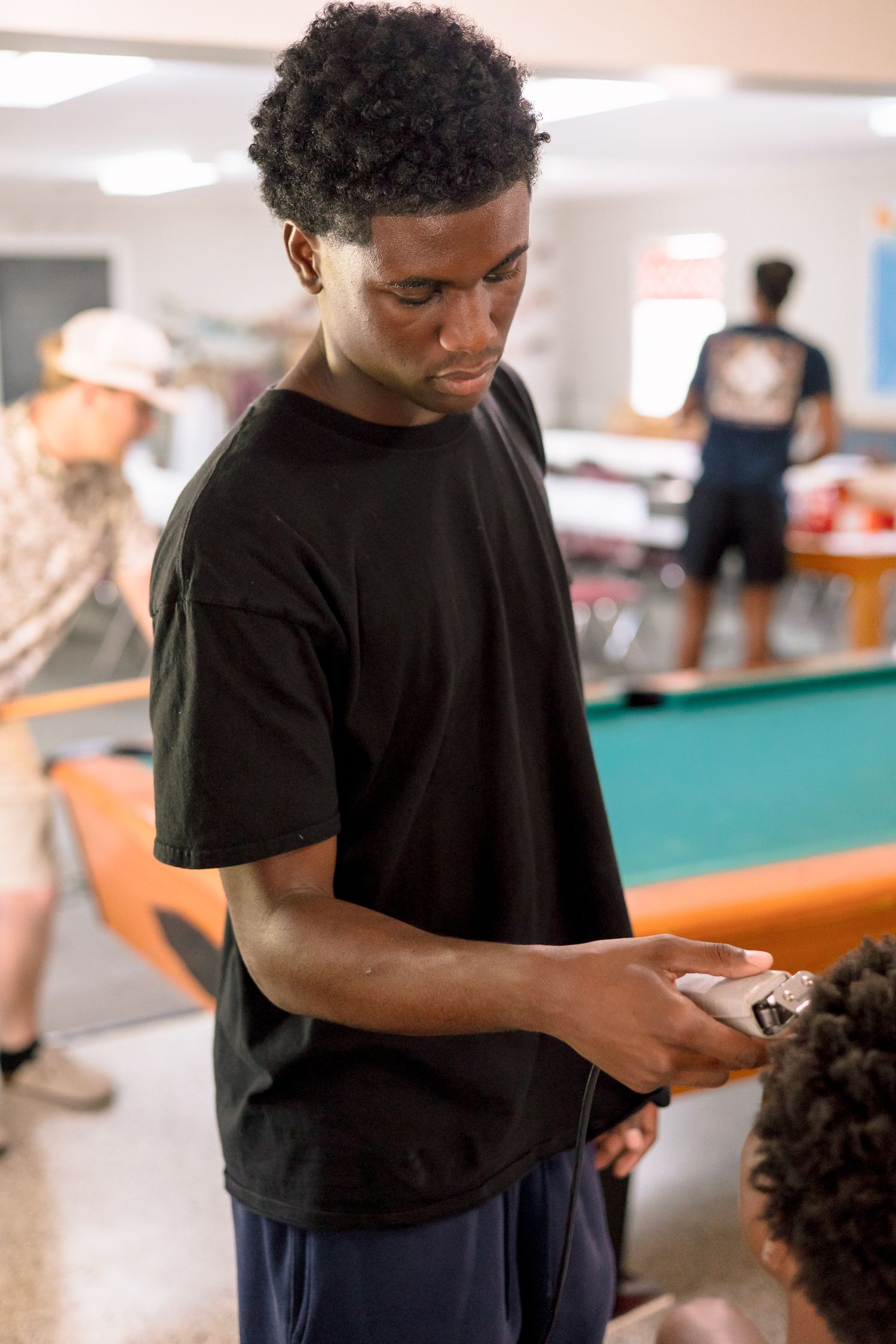 Young man in black t-shirt examining championship ring near pool table in recreation room.