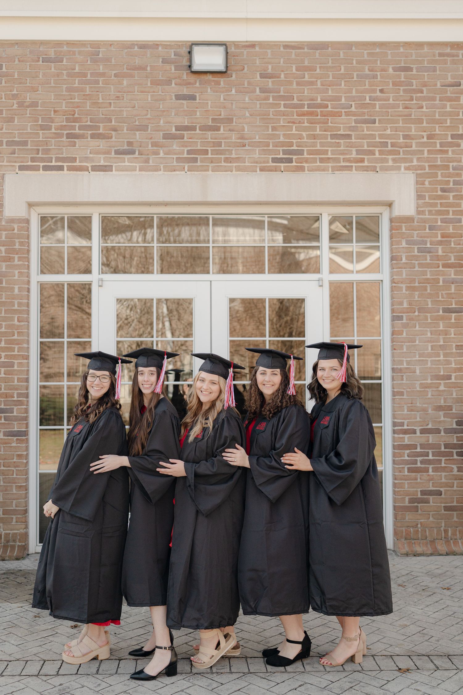 Graduates in black caps and gowns pose together while sitting on steps outside a brick building.