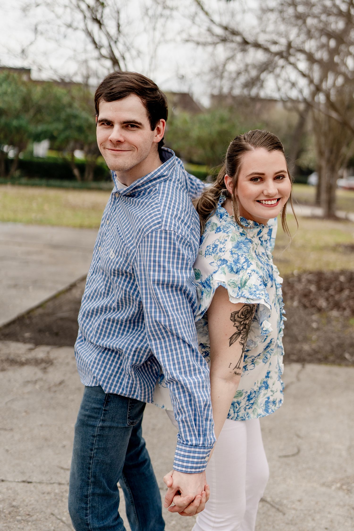 Couple holds hands and laughs while walking together outside in casual blue and white outfits.