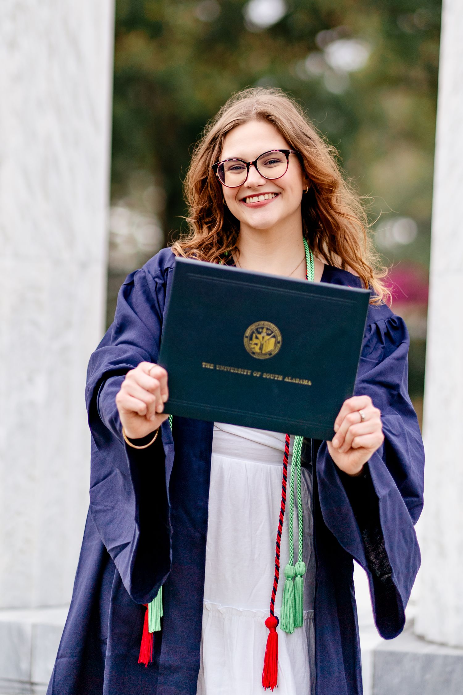 Graduate displays diploma holder with tassels between marble columns.