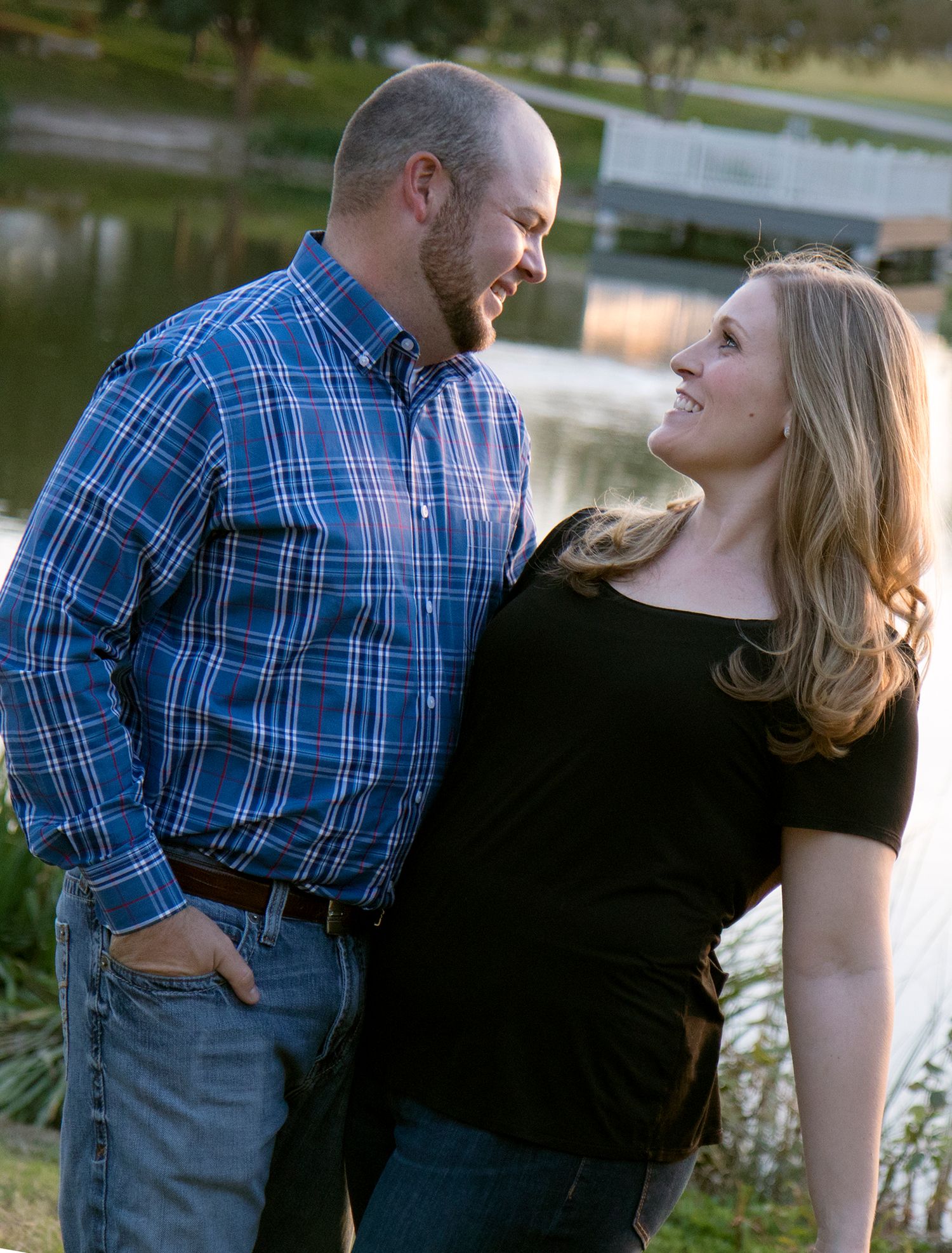 Couple in casual attire sharing intimate moments by a lake at sunset.