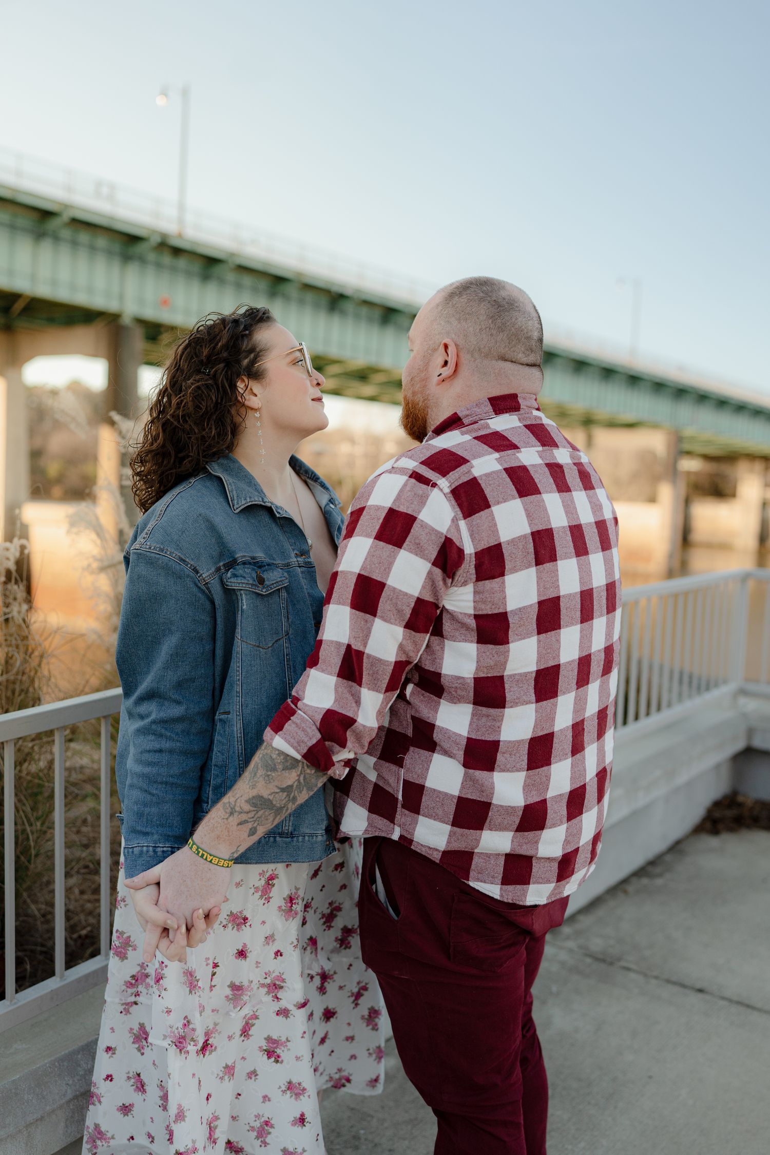 Two people share an intimate moment on a bridge walkway at sunset.