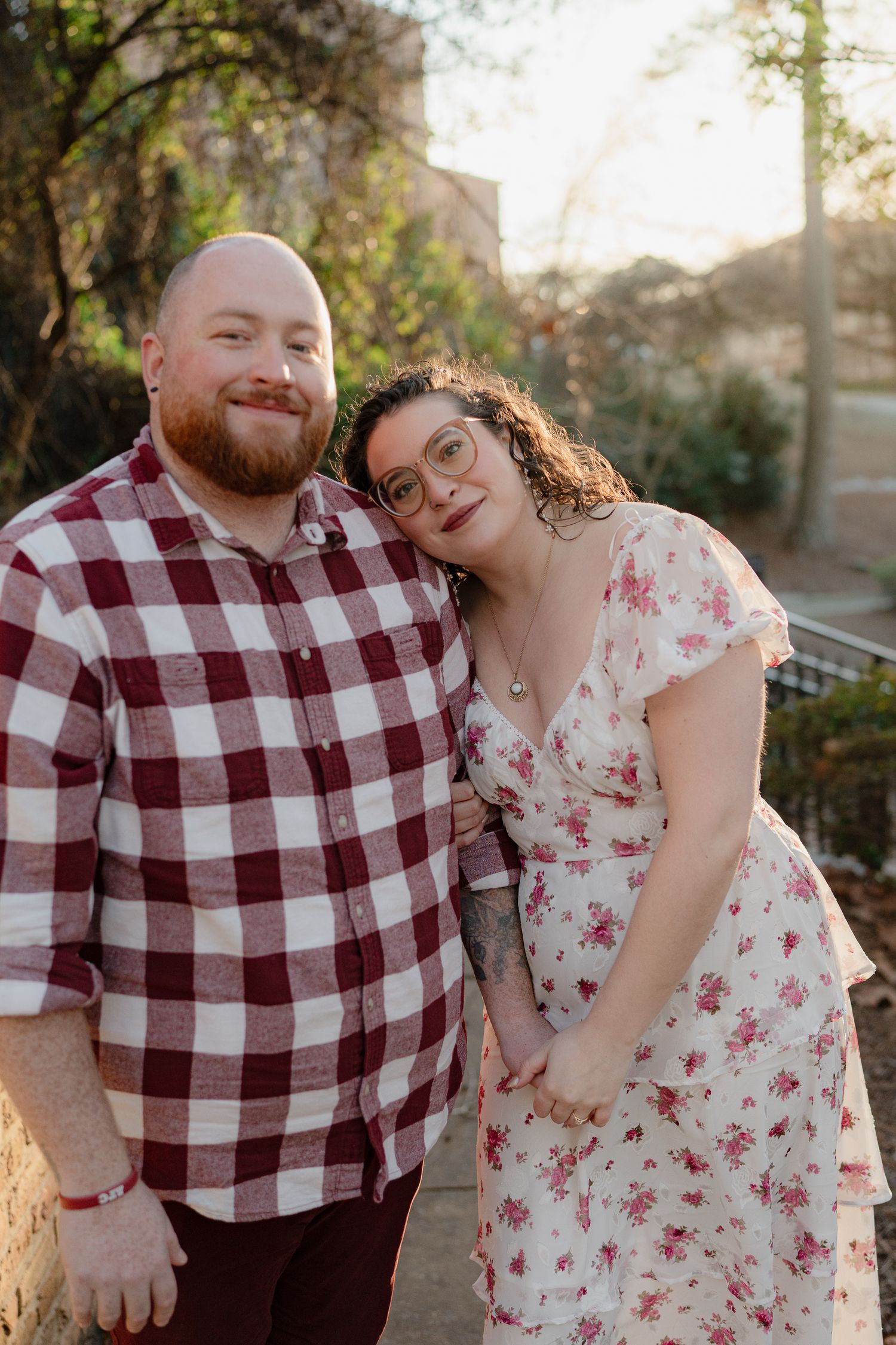 Couple in plaid shirt and floral dress share intimate moments during sunset photo session in park.