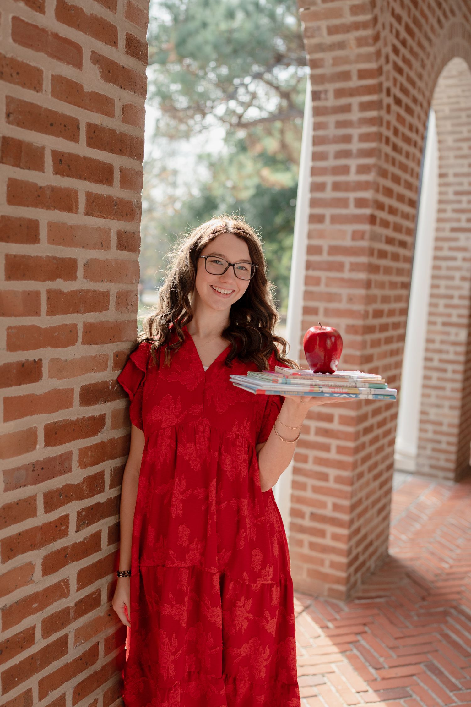 Someone in a red dress and glasses holds a serving tray with a beverage while standing in a brick archway.