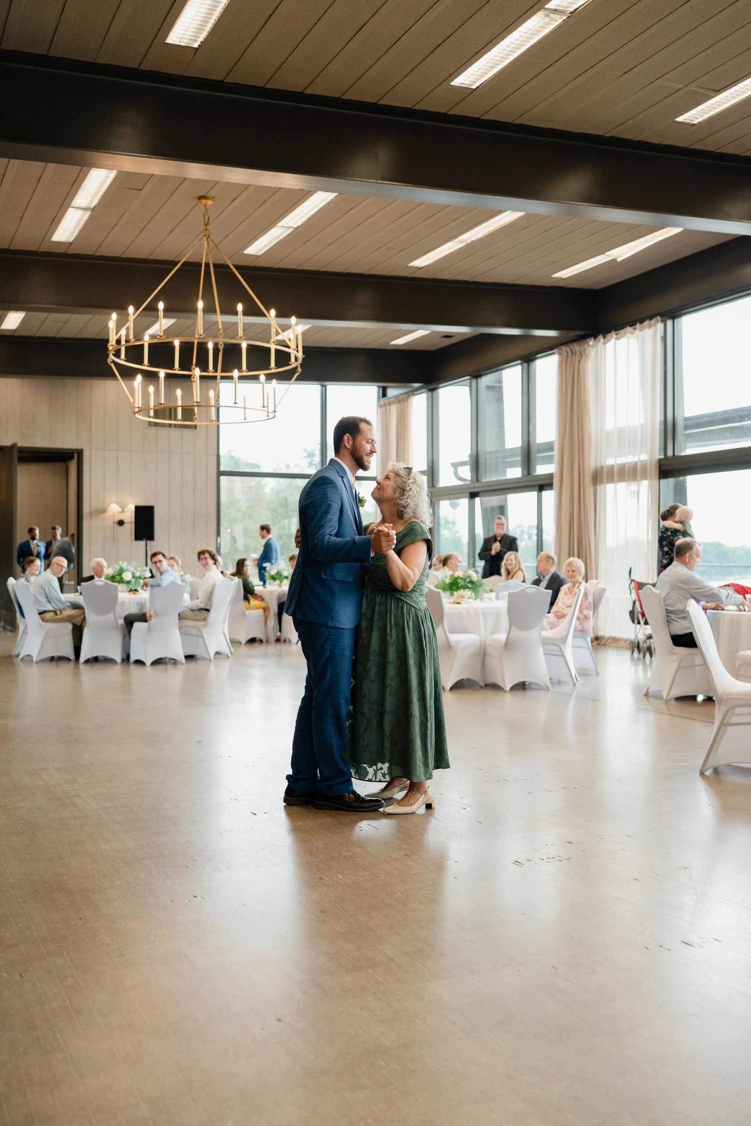 A large empty event space with chandeliers and white chairs arranged for a special occasion.
